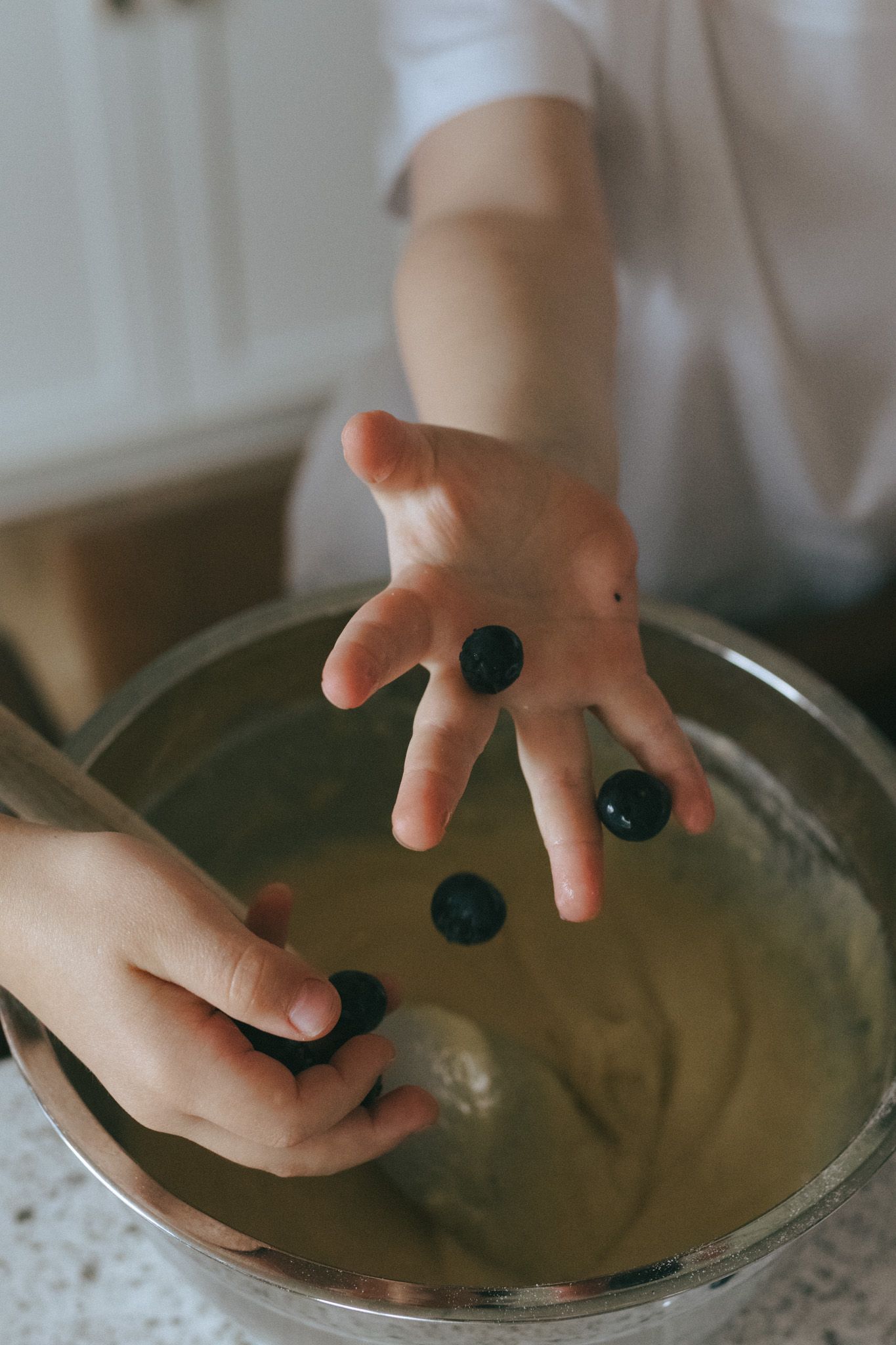 Child's hands dropping blueberries into bowl.