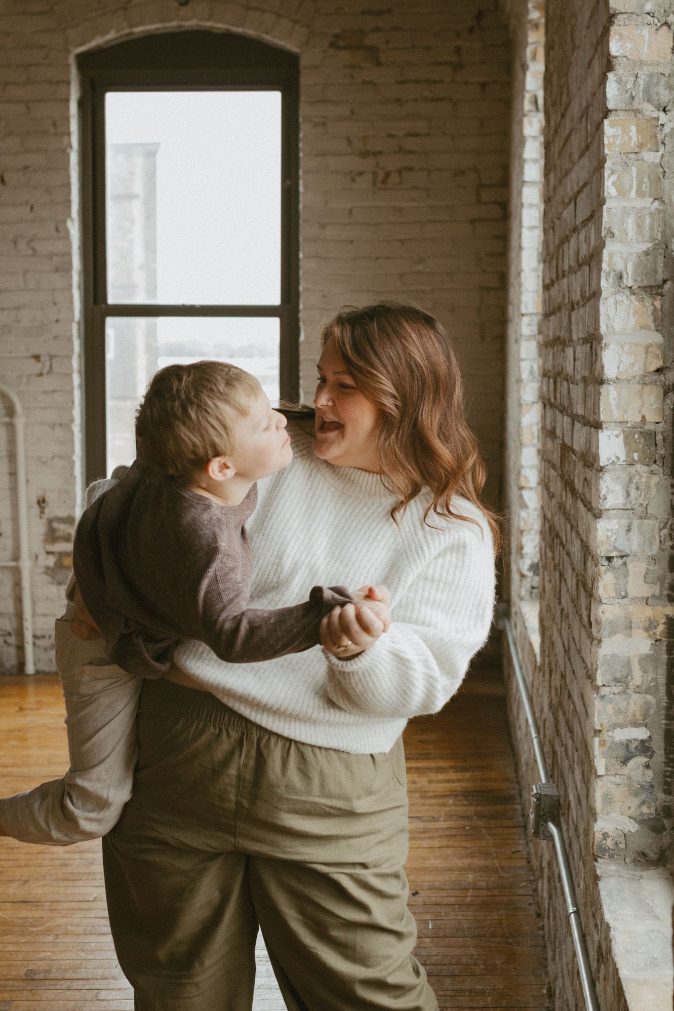 Mother laughing joyfully while holding her young child in a bright loft space.