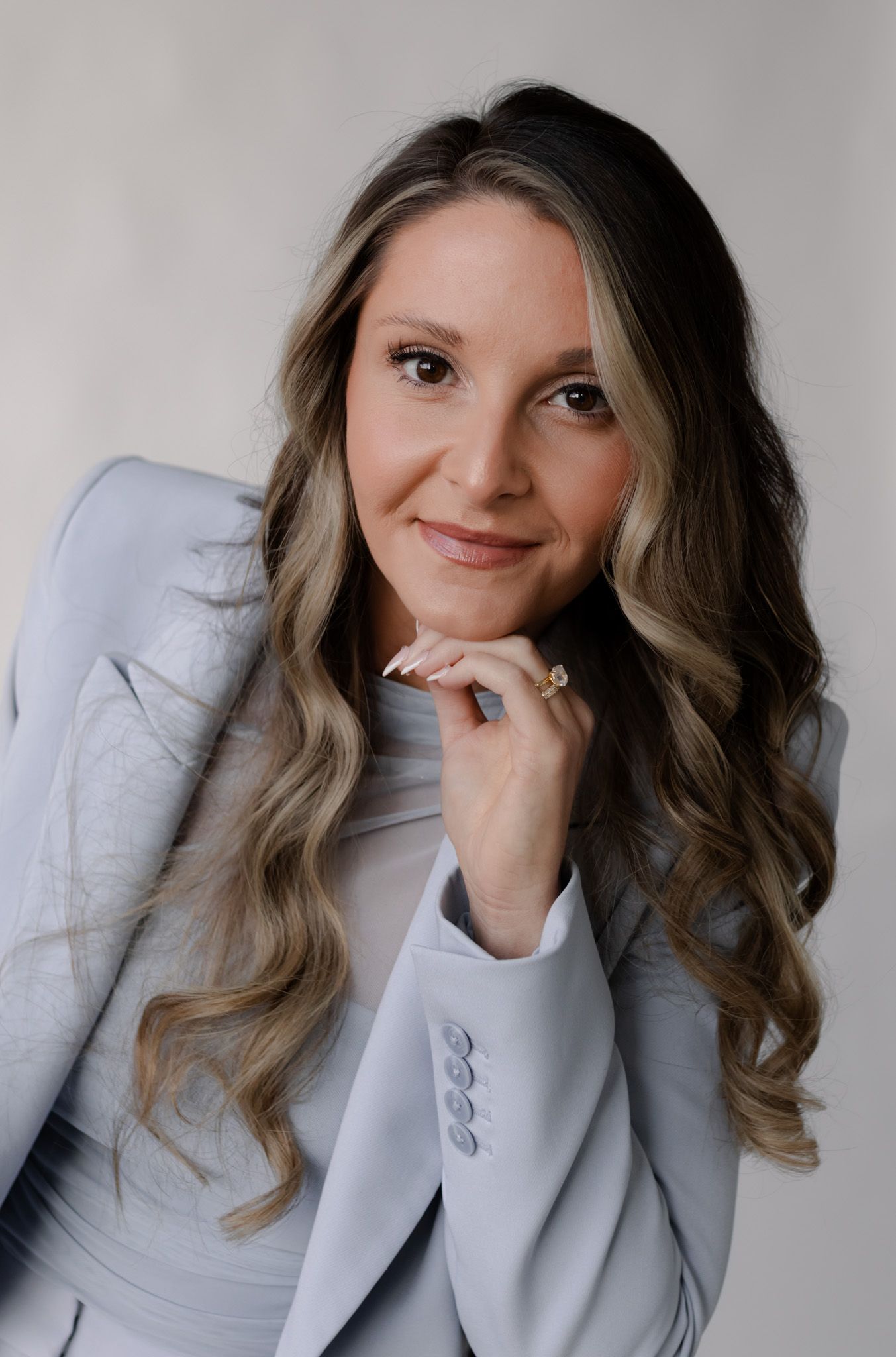 Professional woman in light gray blazer posing confidently against neutral background.