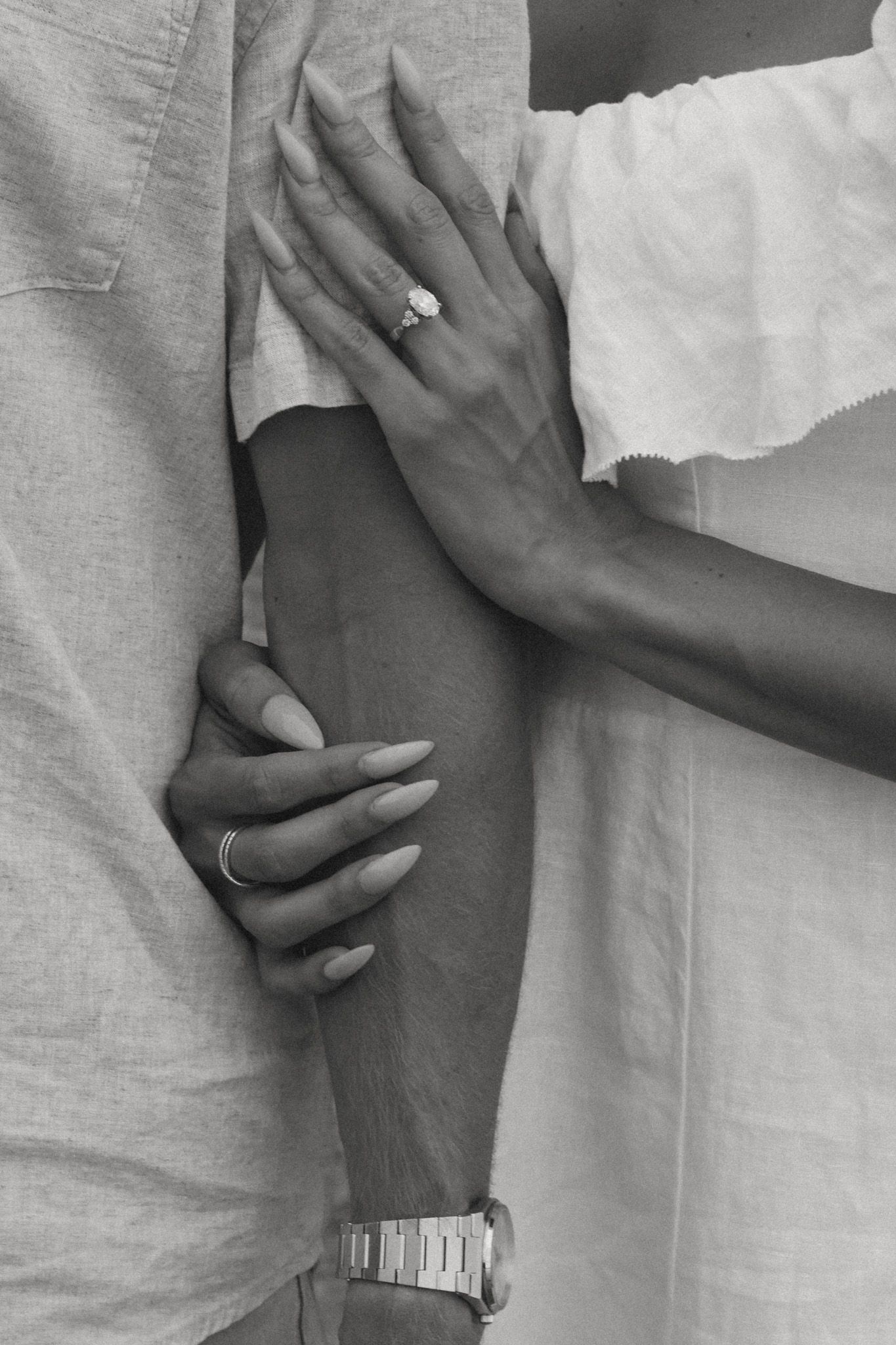 Black and white close-up of couple embracing, woman wearing diamond engagement ring and watch.