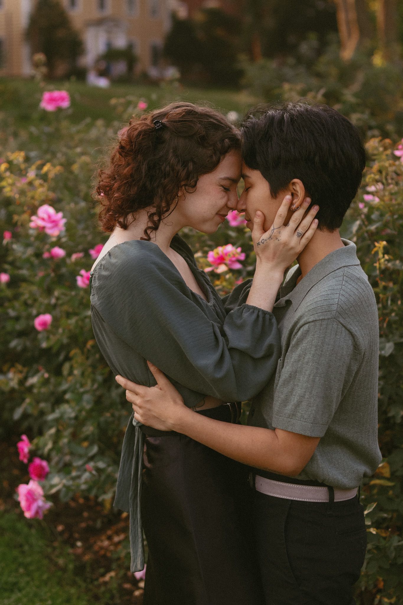 Couple sharing a romantic moment in a rose garden, foreheads touching, surrounded by pink blooming roses in Minneapolis.