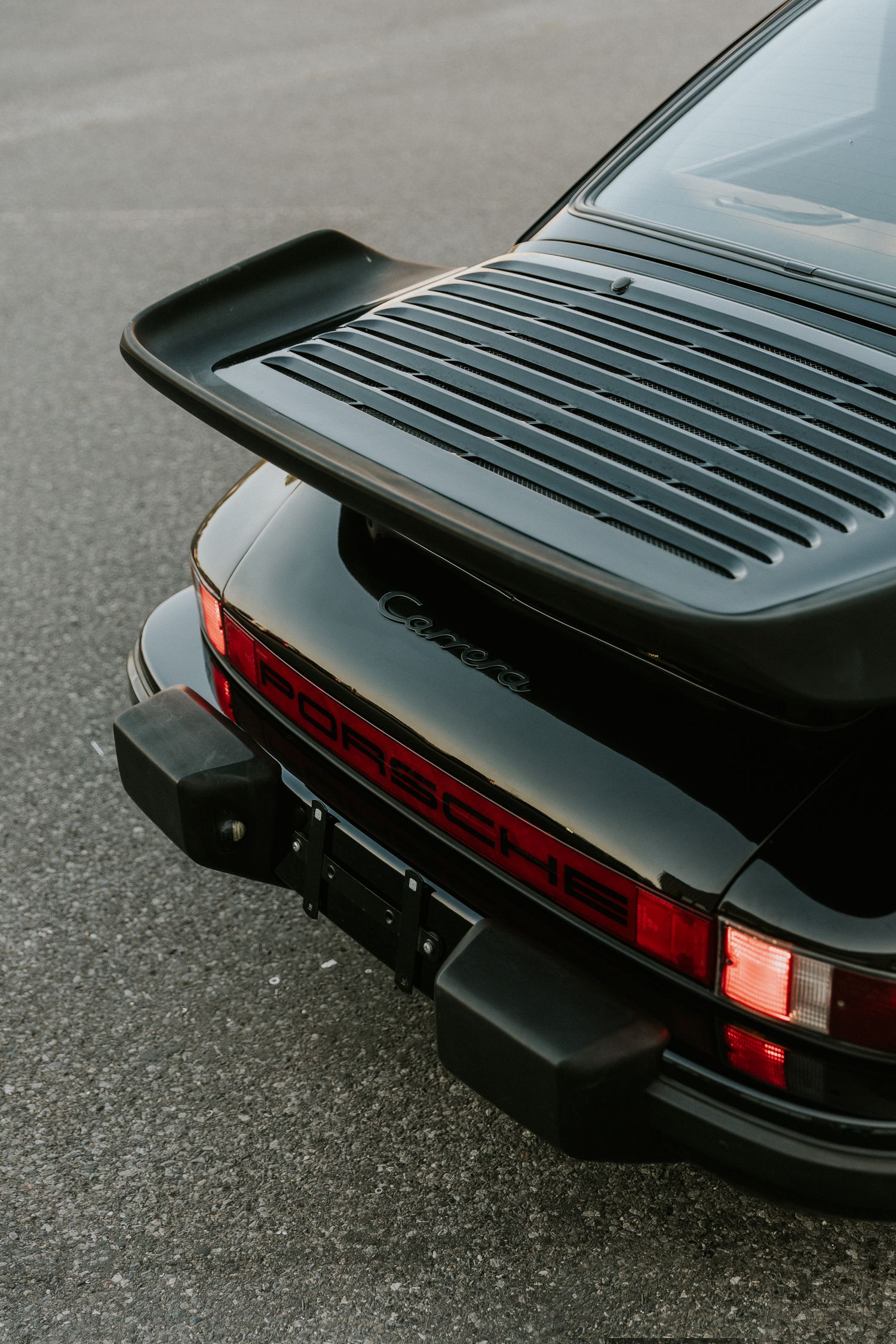 Rear view of a classic black Porsche 911 Carrera showing iconic ducktail spoiler and red taillights.