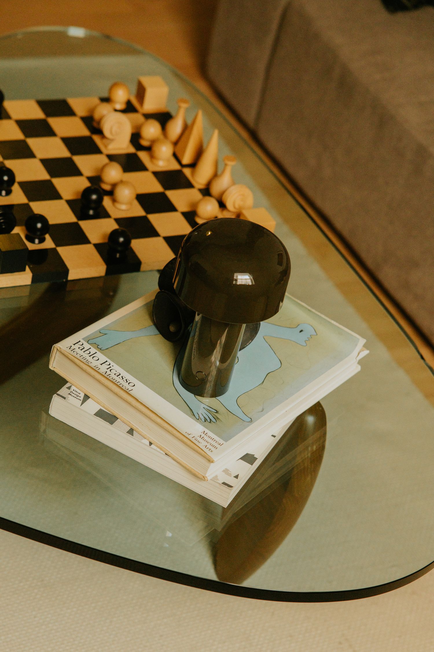 Glass coffee table with chess board, Pablo Picasso books, and a black mushroom lamp on top.