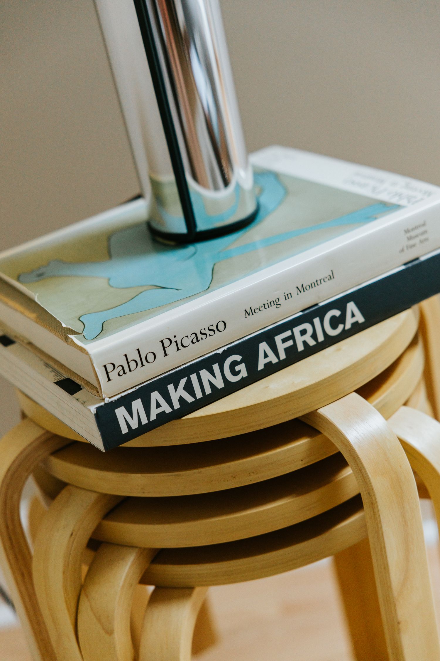 Two art books, Pablo Picasso and Making Africa, stacked on a wooden stool with a chrome lamp.