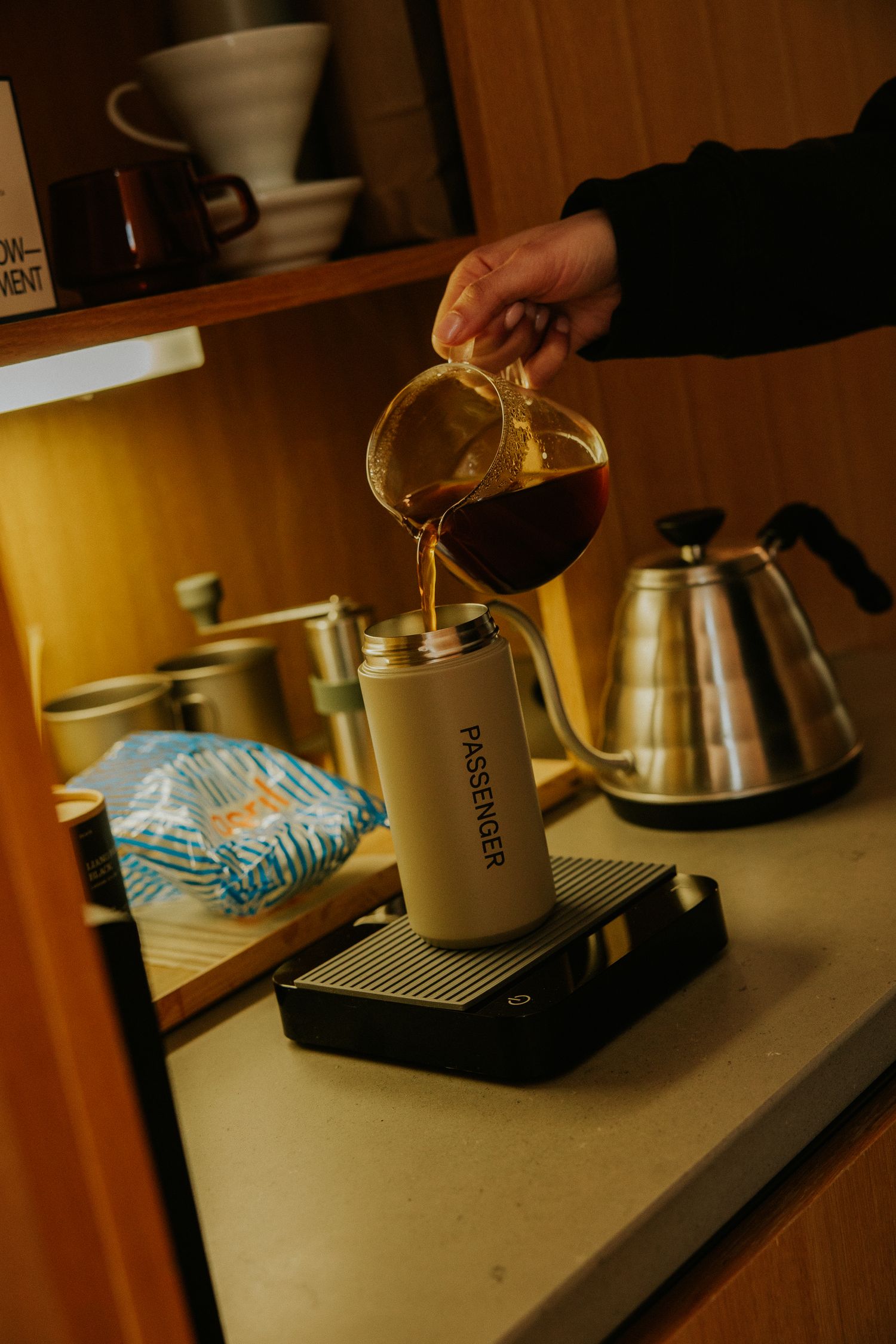 Hand pouring coffee into Passenger travel mug on scale in warm kitchen.