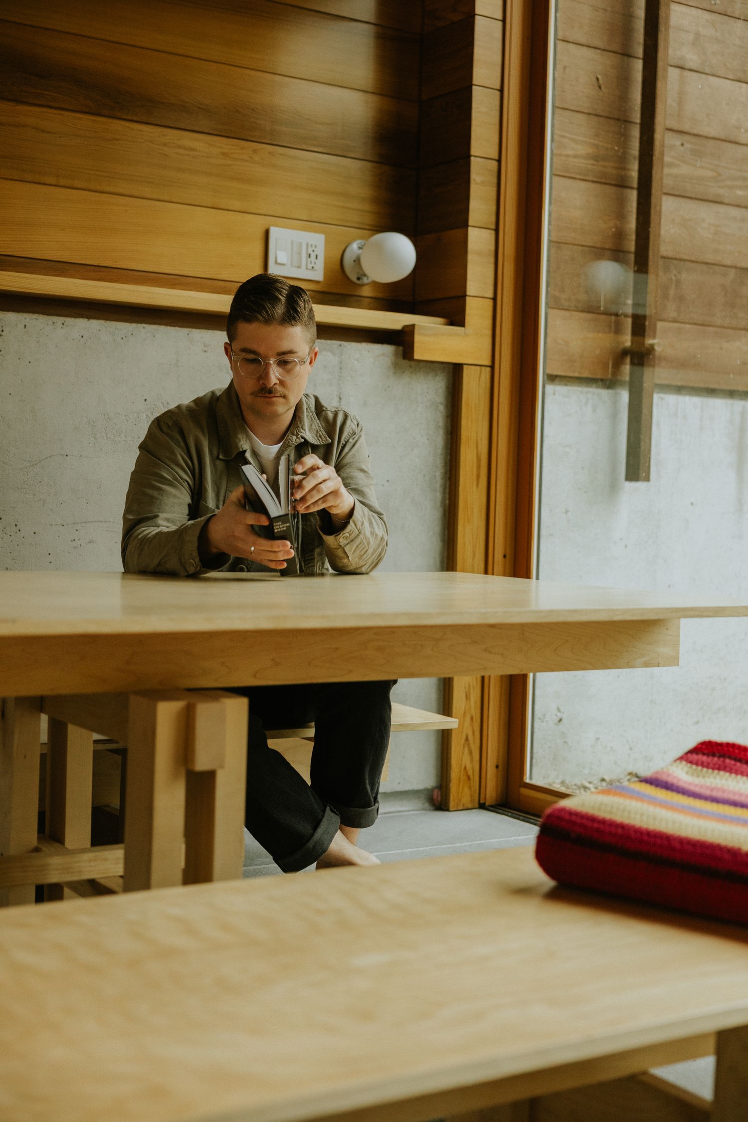 Man with glasses sitting at wooden table examining camera in modern interior.