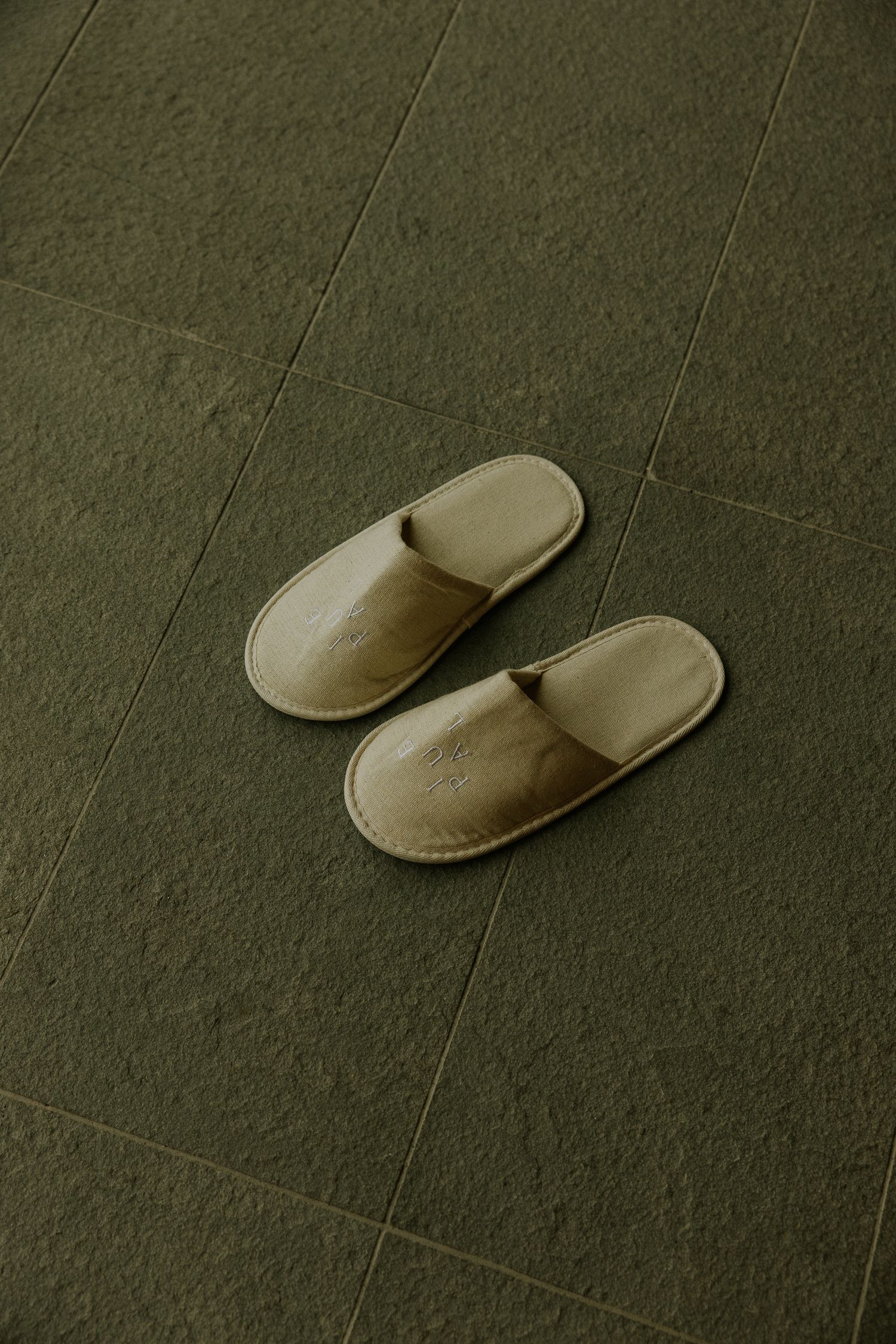 Beige leather slippers placed on green tiled floor, minimalist hotel room footwear.