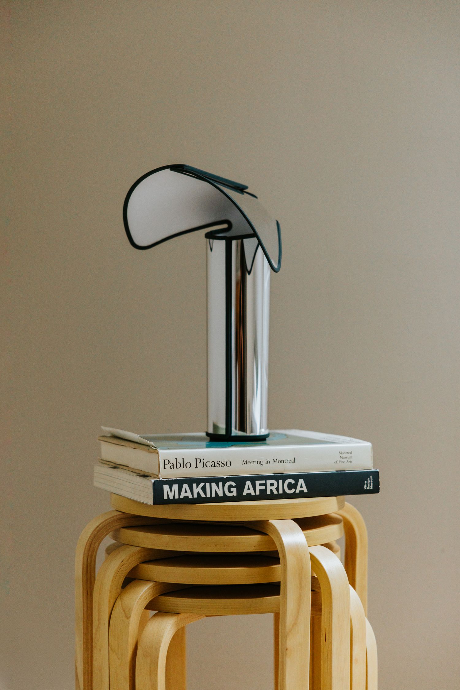 Chrome designer lamp balanced on Pablo Picasso and Making Africa books atop a wooden stool.