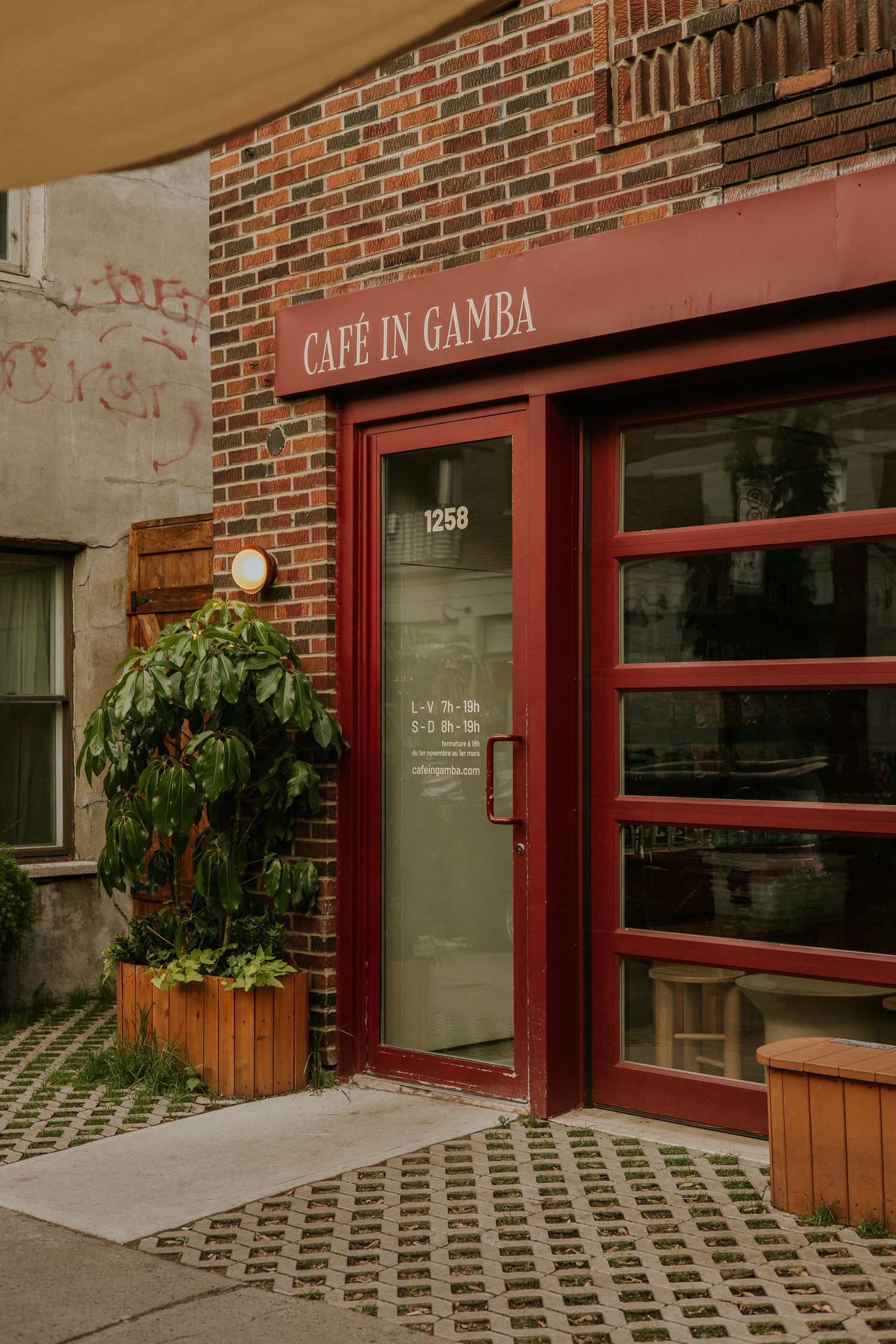 Exterior of Cafe in Gamba brick building with red door and green plants at entrance number 1258.