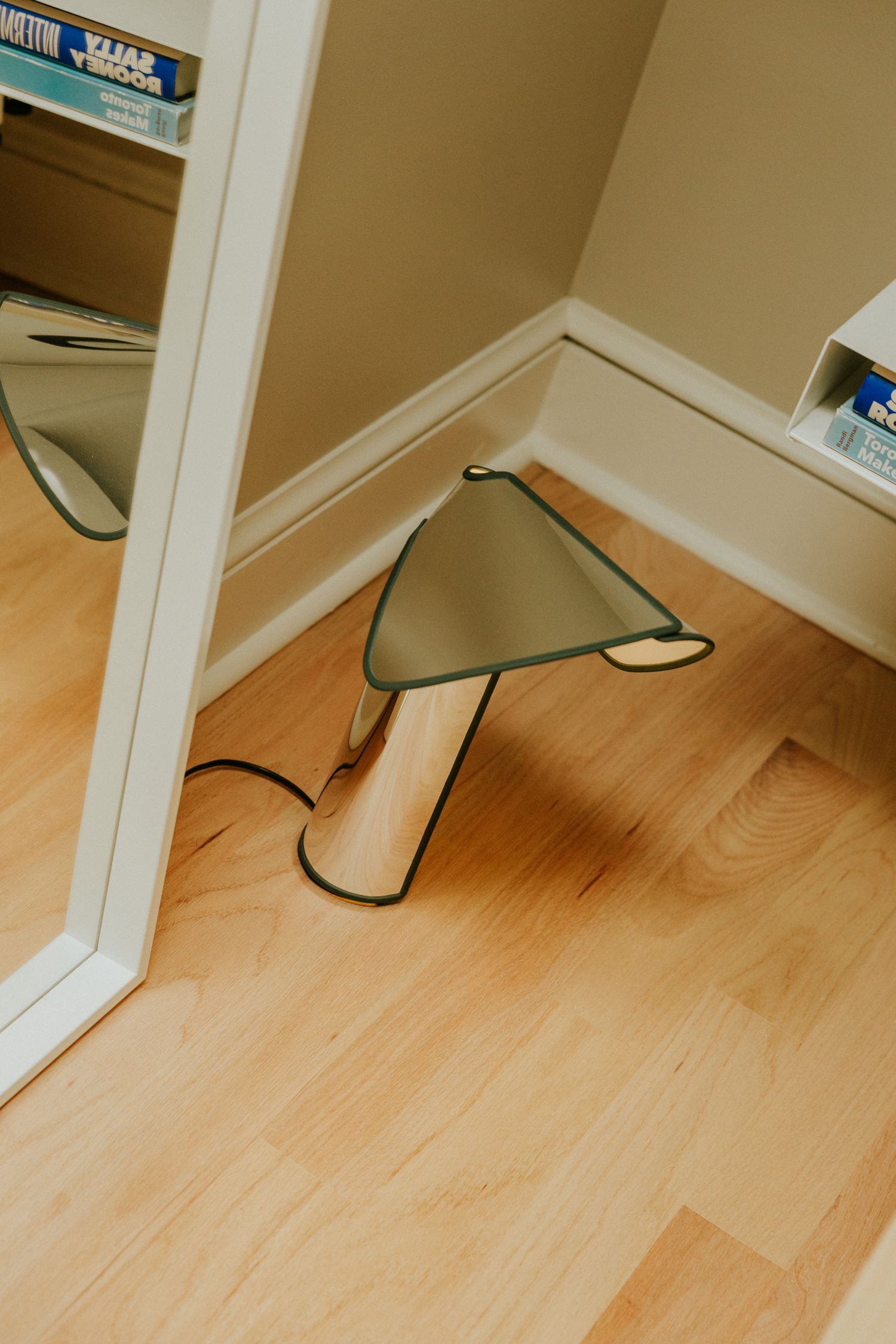Modern mushroom-shaped green glass table lamp on hardwood floor beside a mirror.