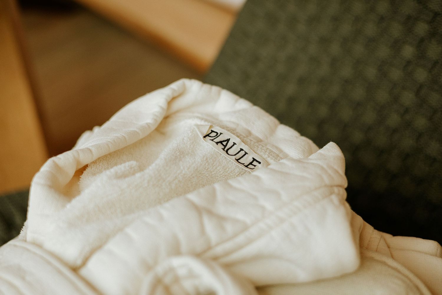 White monogrammed bathrobe with PAULE embroidery, folded neatly on a green chair in a hotel room.