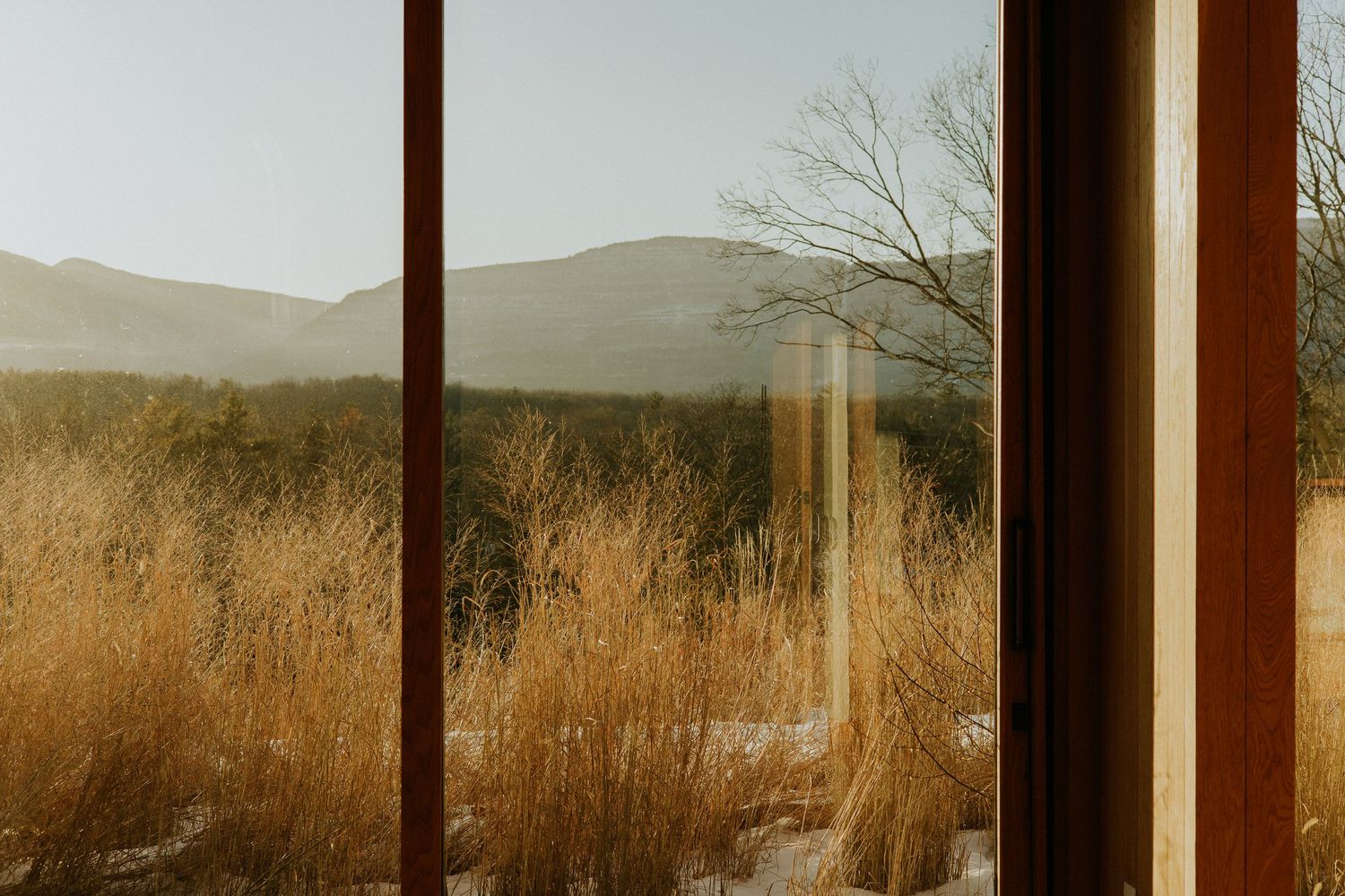 Golden hour view of mountain landscape and dry grassland through large window.