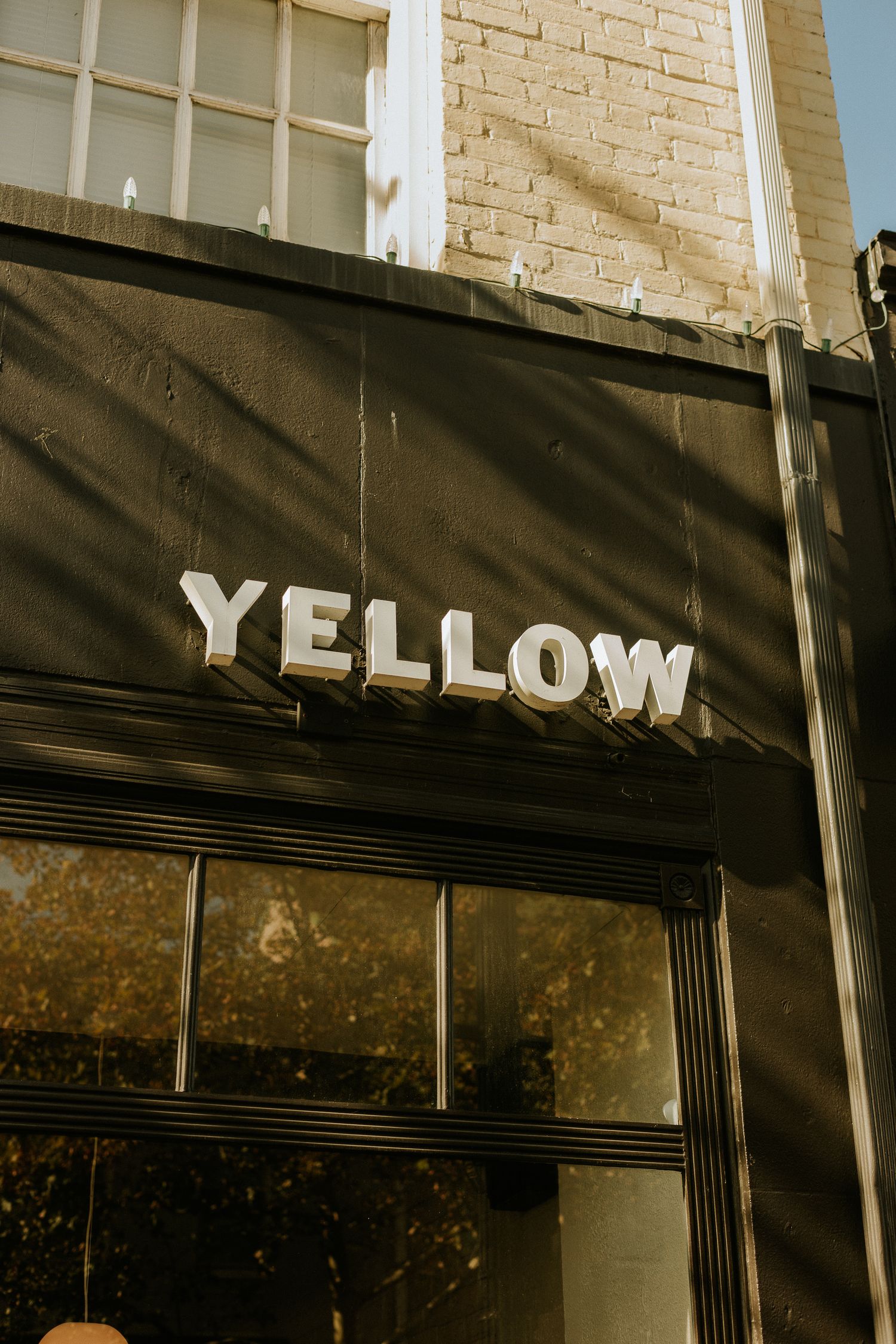 Storefront with bold white YELLOW lettering on dark awning with brick building background in sunlight.