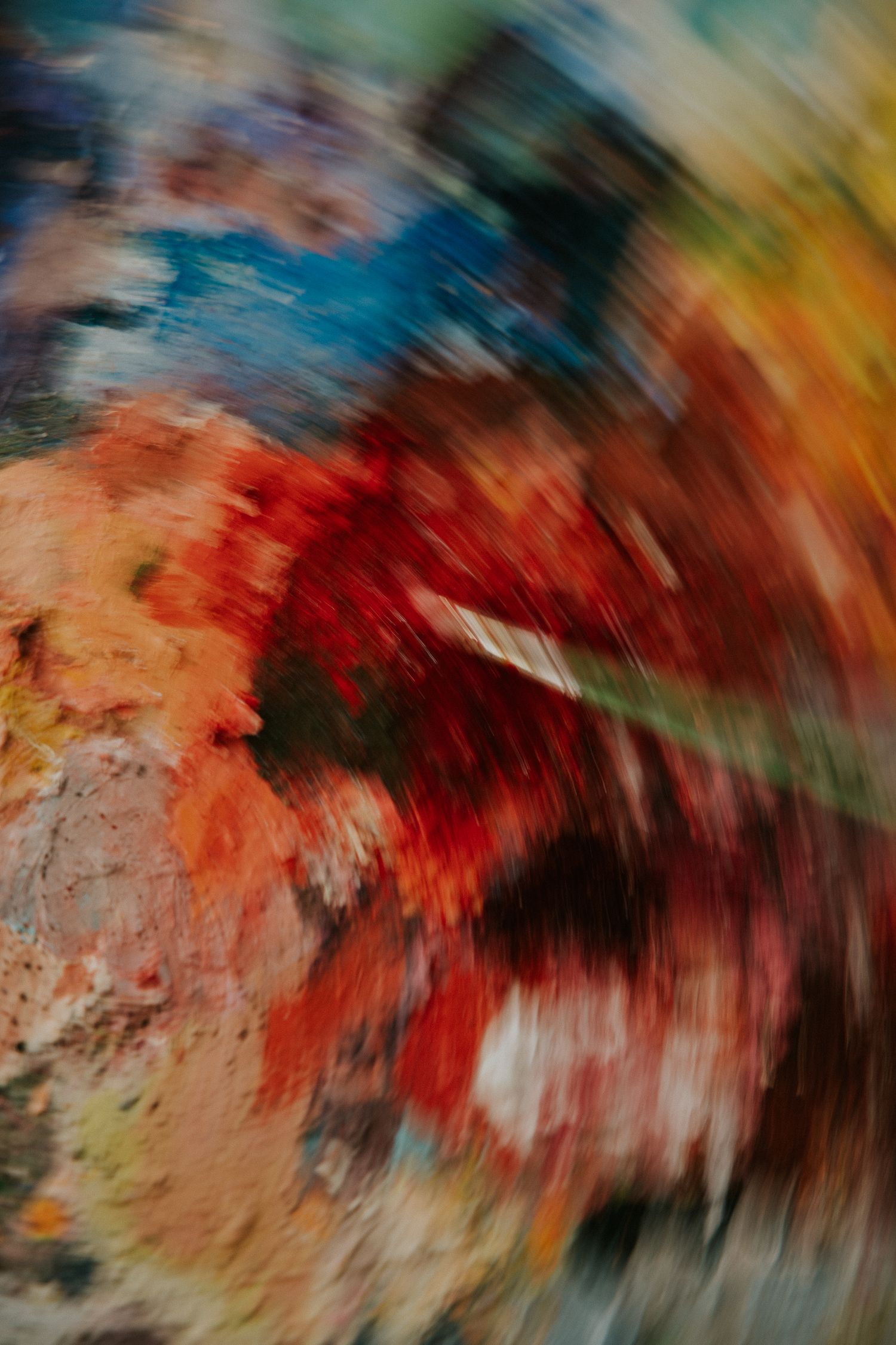 Abstract swirling paint artwork with vibrant red, orange, blue, and earth tones in a dynamic radial blur effect.