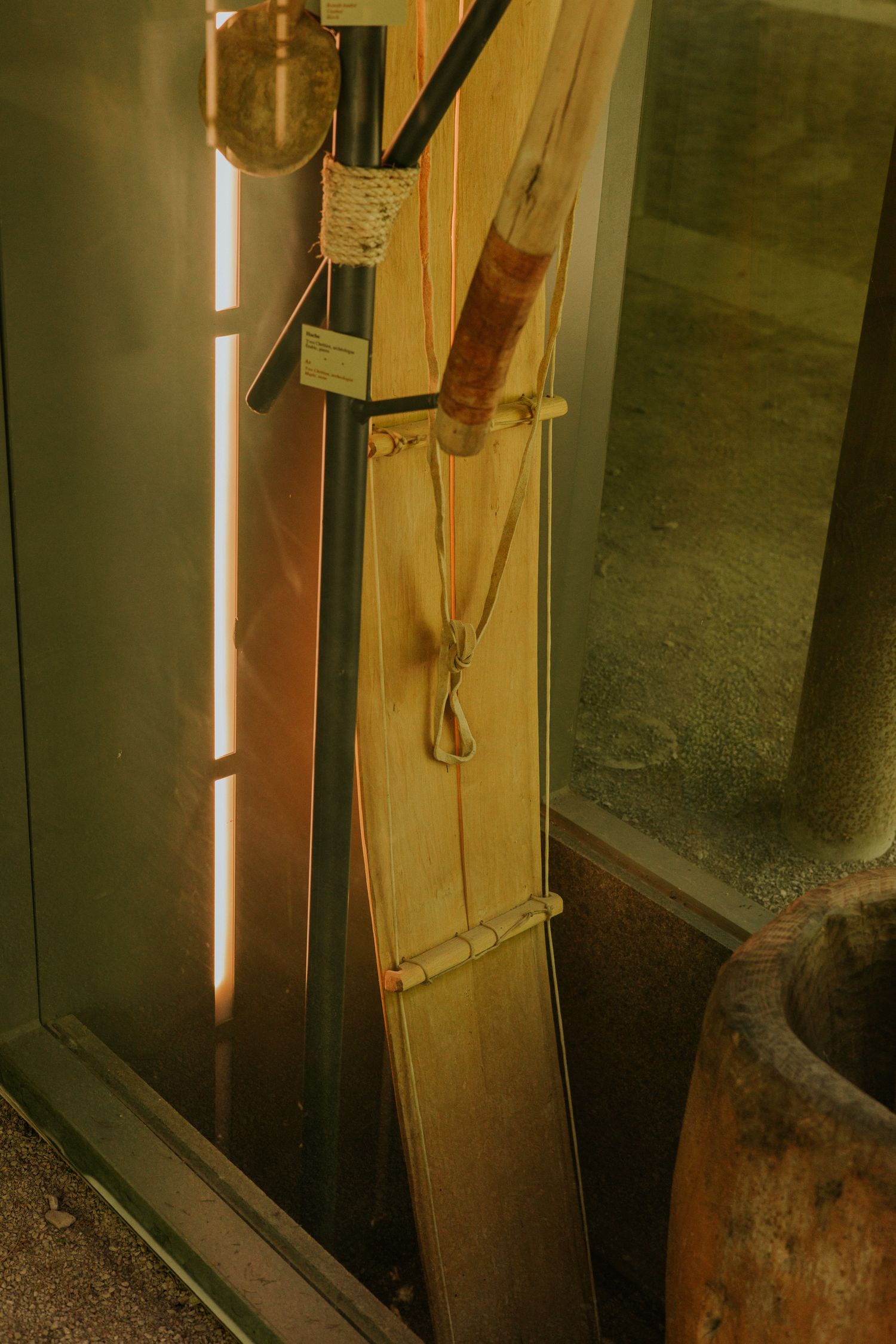 Traditional wooden paddles and tools leaning against a glass display case in warm museum lighting.