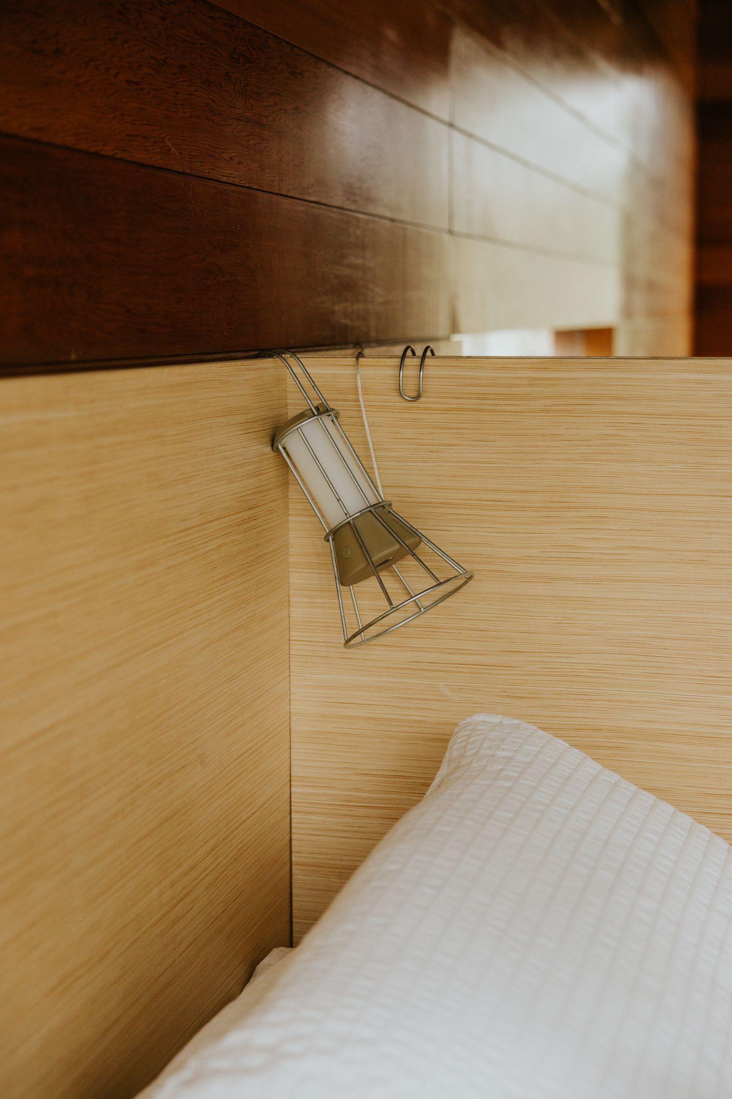 Industrial cage pendant bedside reading lamp hanging on light wood headboard above white pillow.