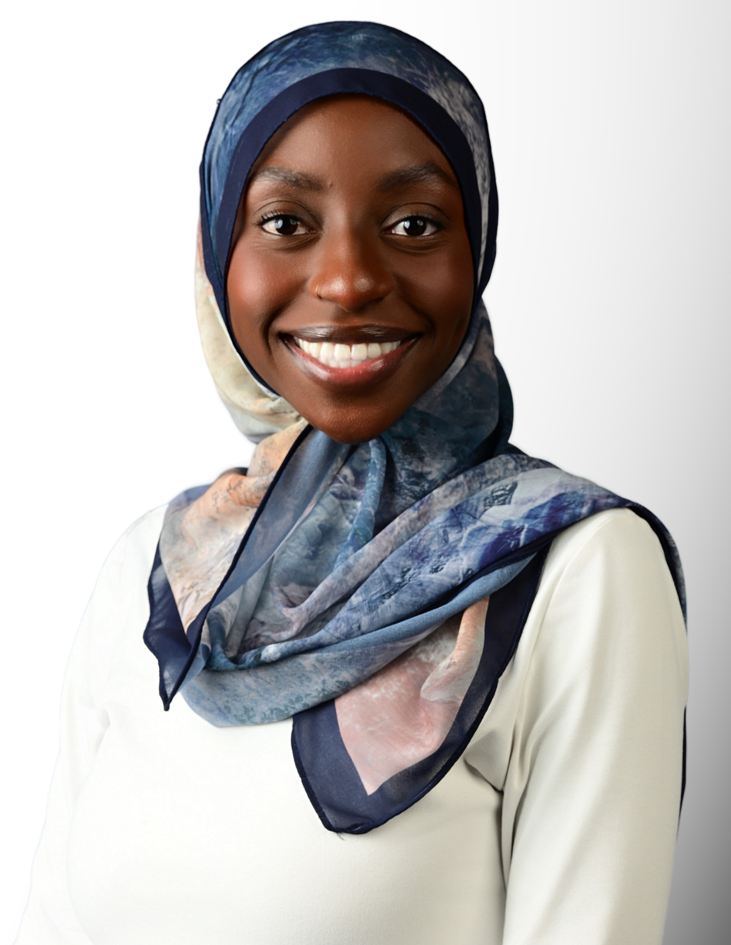 Smiling young woman wearing a navy blue and floral hijab with a cream top against a white background.