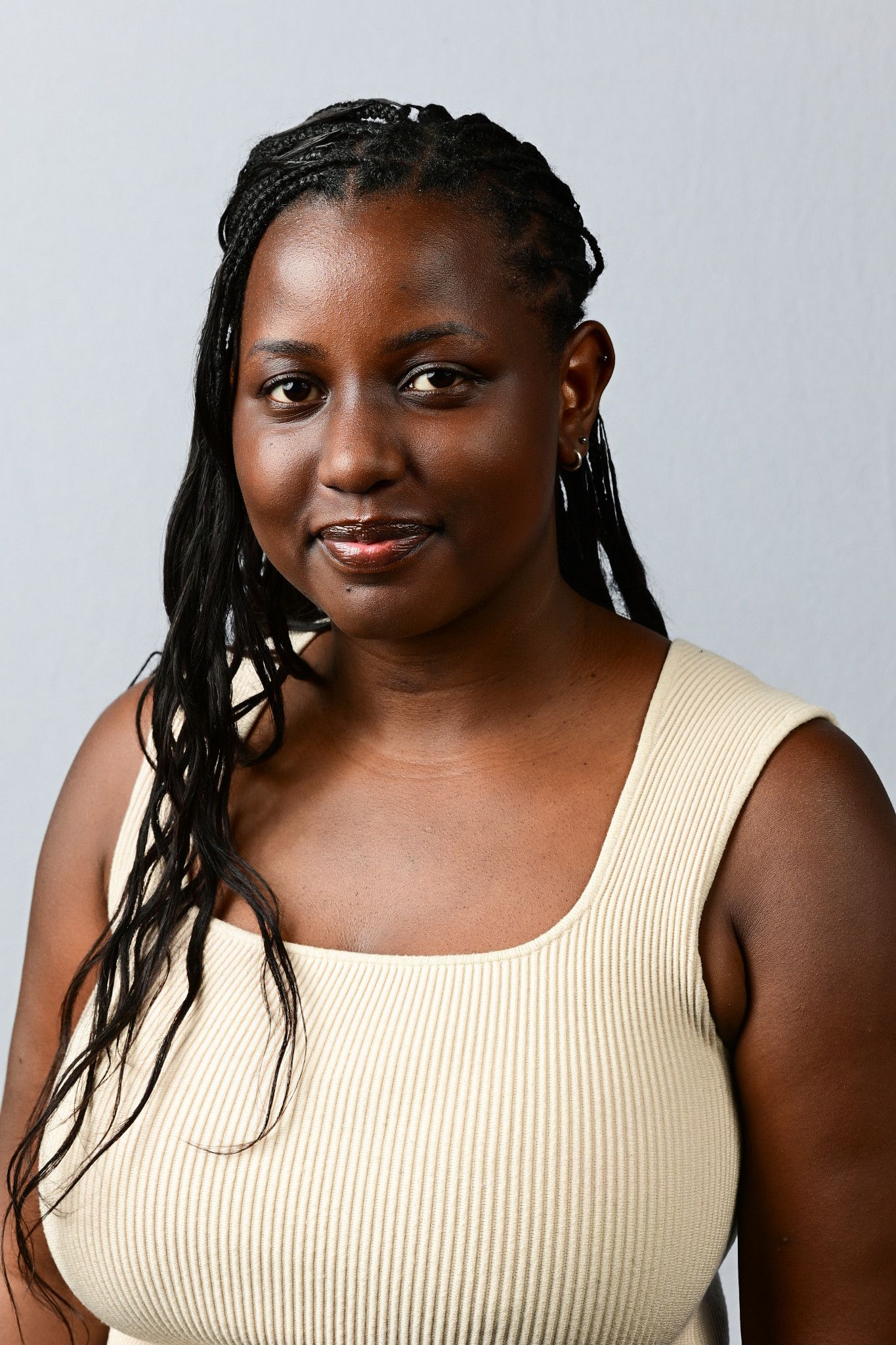 A young Black woman with braided hair wearing a cream sleeveless top, smiling confidently against a gray background.