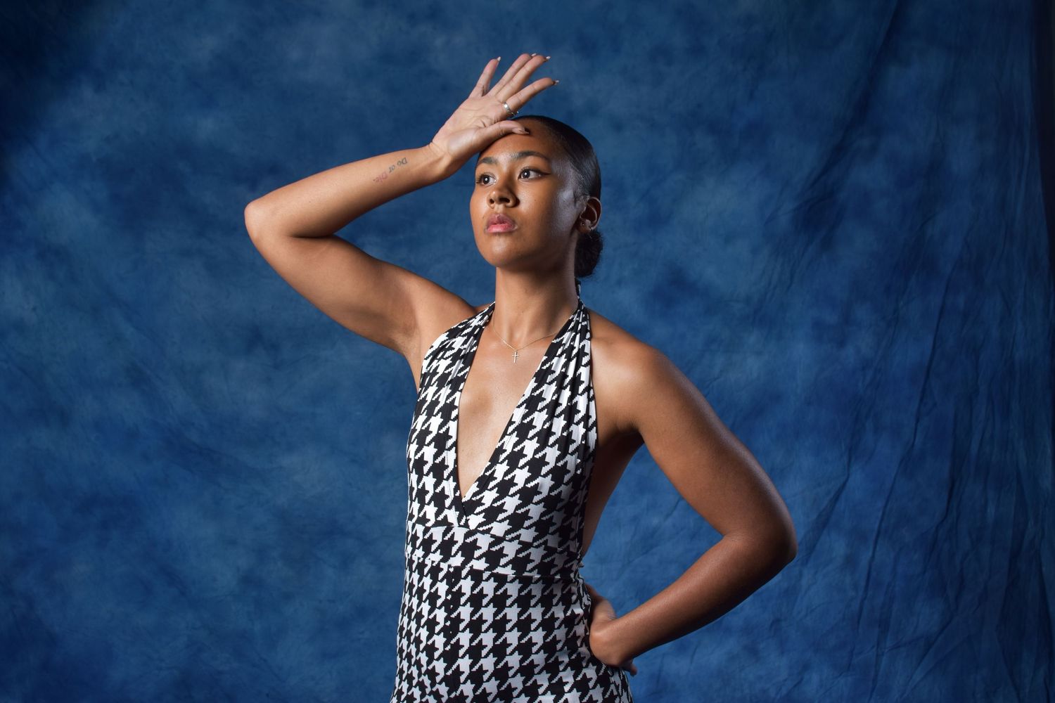 Black woman in houndstooth halter dress poses dramatically against blue textured studio backdrop.