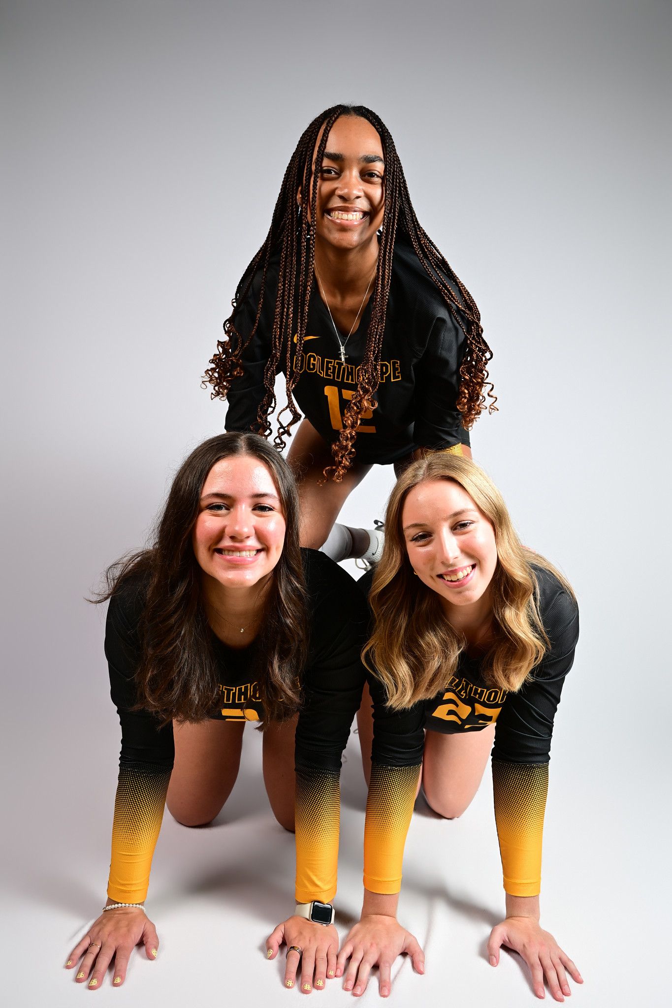 Three Oglethorpe University female athletes pose together in black and gold uniforms for a team photo.