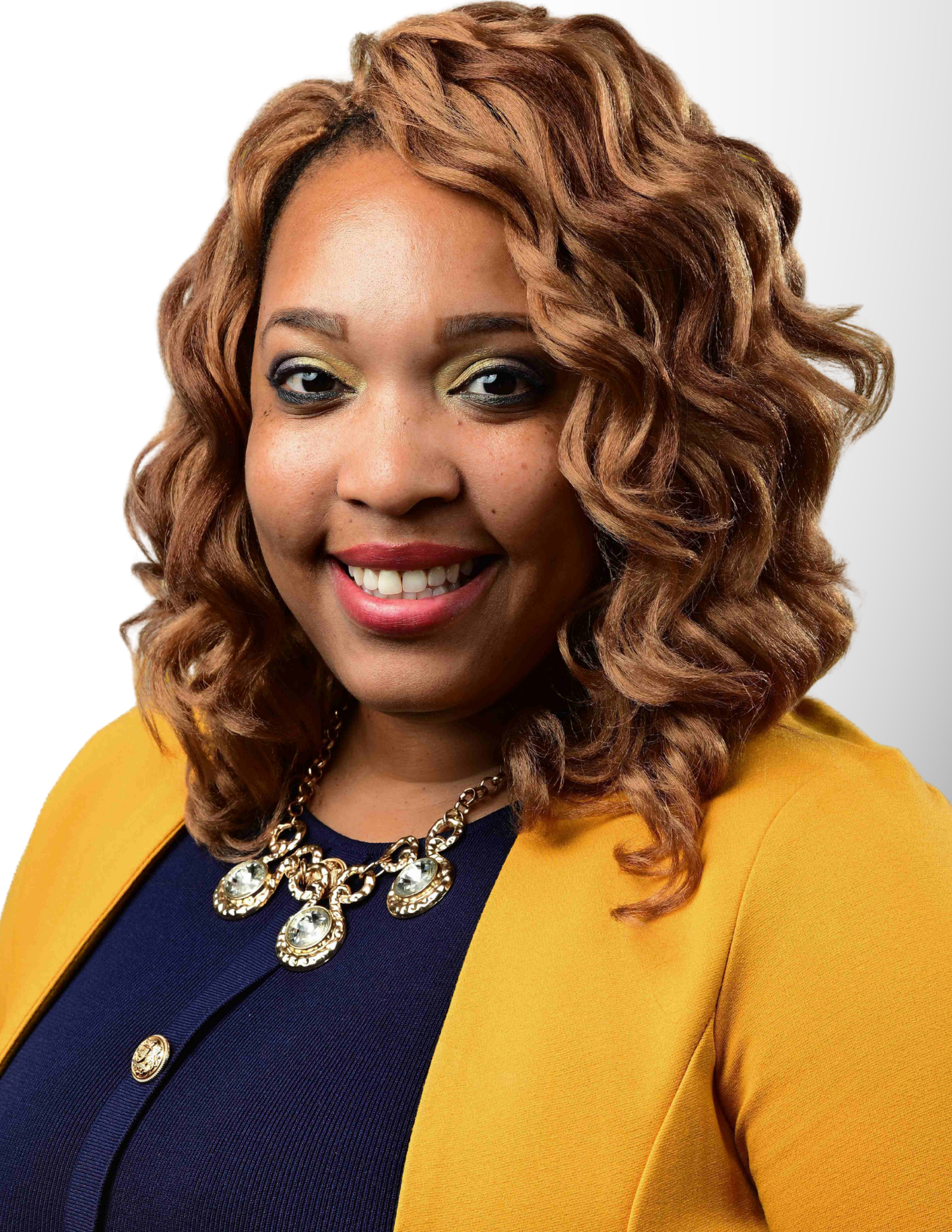 Professional woman smiling in a mustard yellow blazer and statement necklace with curly auburn hair.