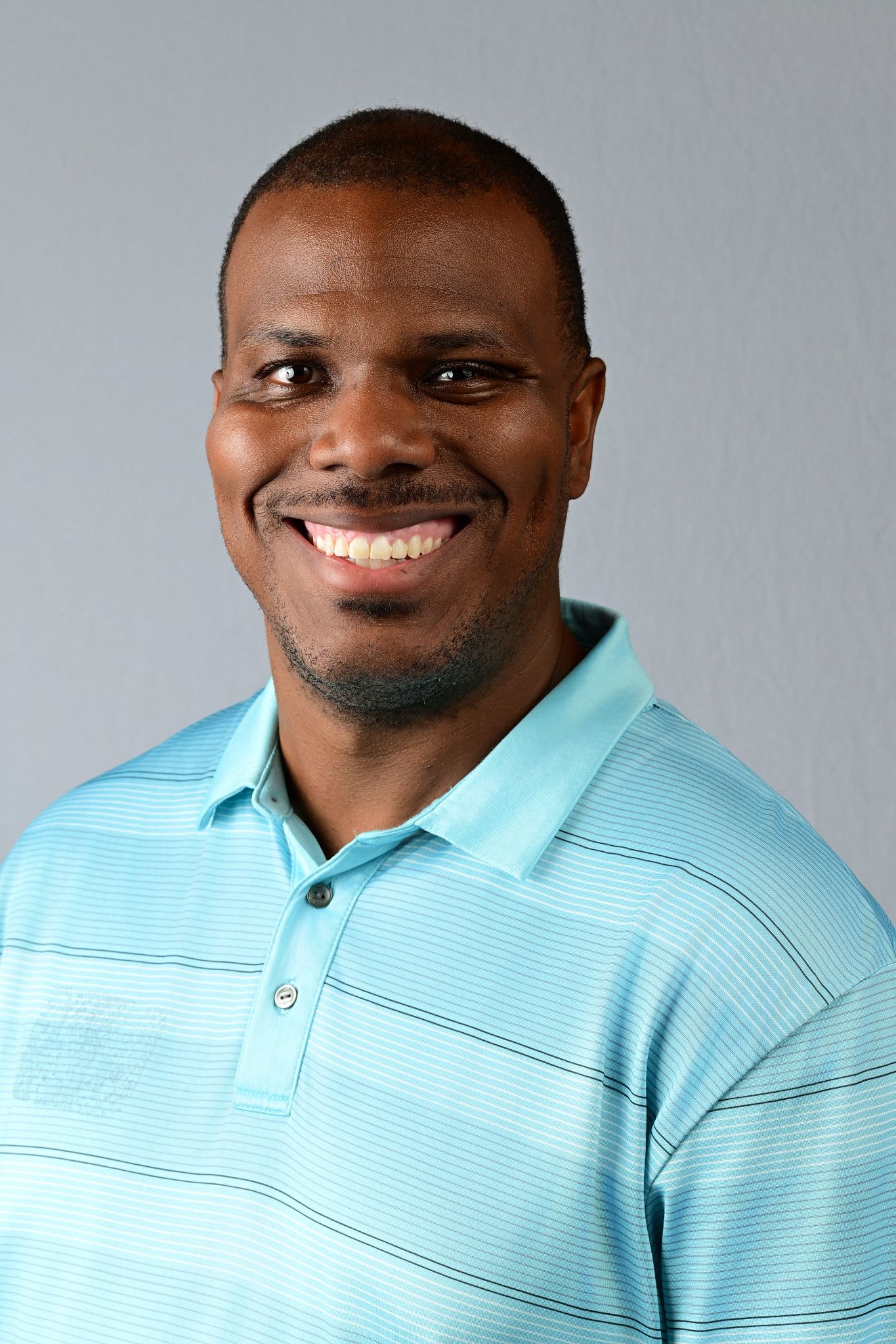 Smiling Black man in a light blue striped polo shirt poses for a professional headshot photo.