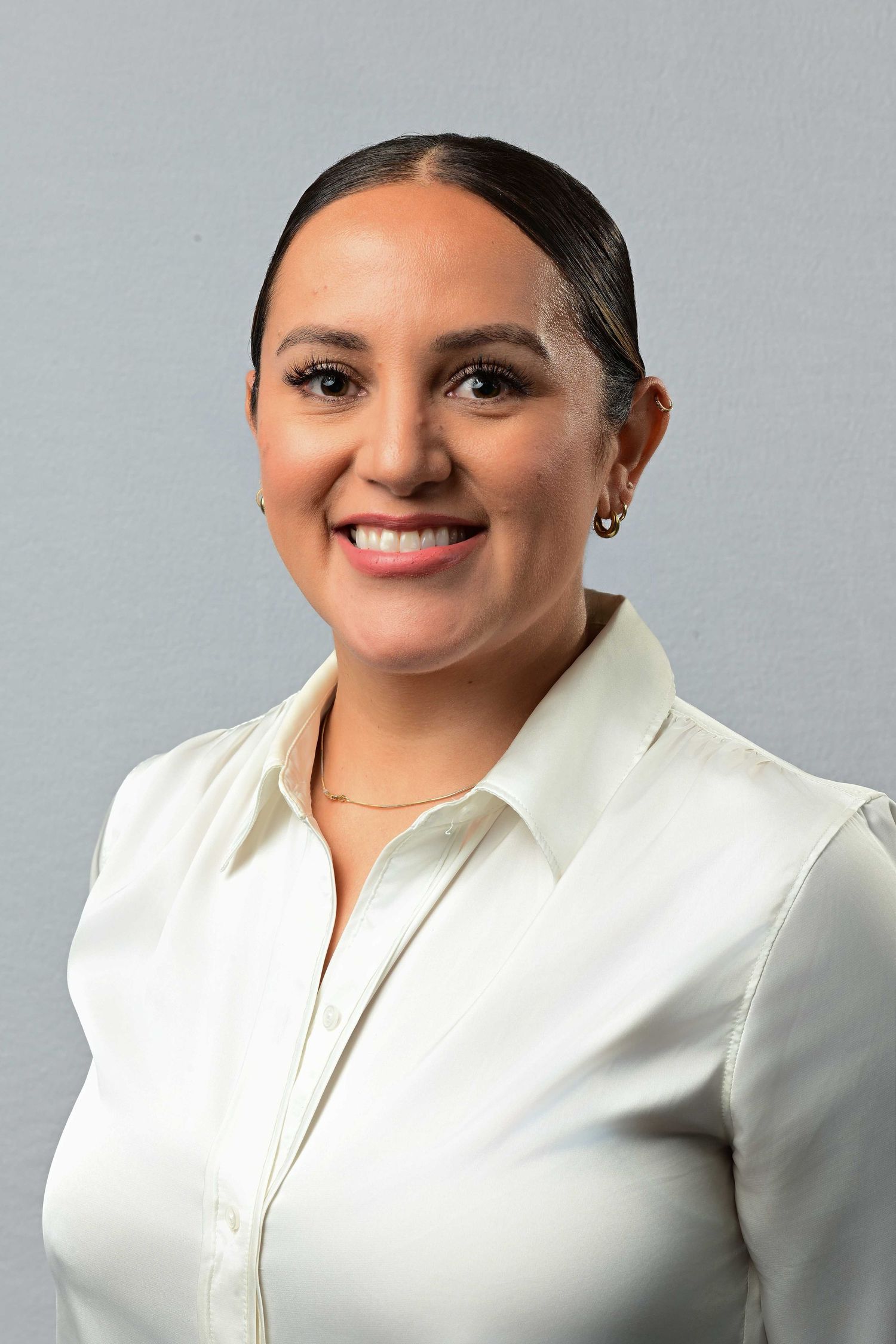 Professional headshot of a smiling young woman in a white button-up shirt against a gray background.