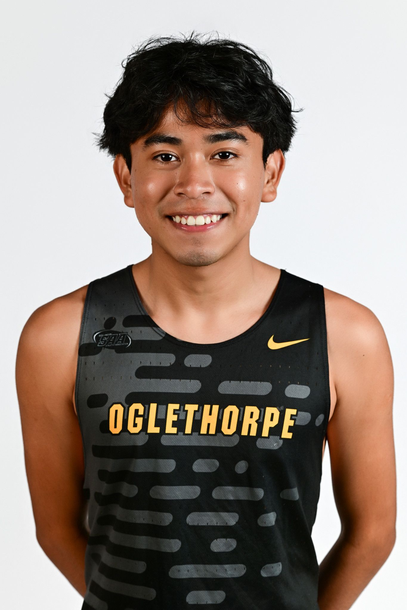 Oglethorpe University male track athlete smiling in black and gold Nike uniform against white background.