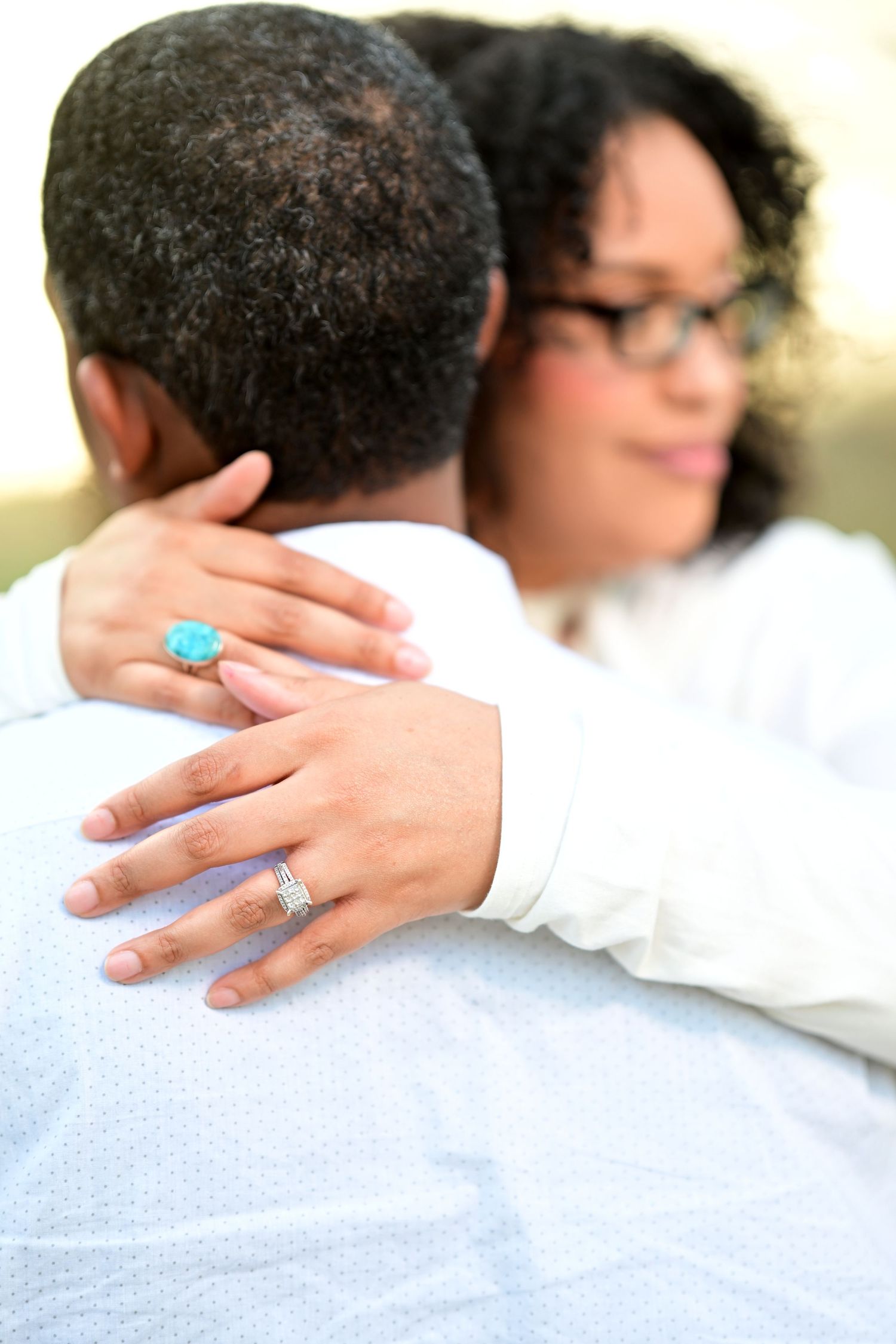 A couple embraces closely, showcasing a turquoise ring and diamond band on the woman's hand.