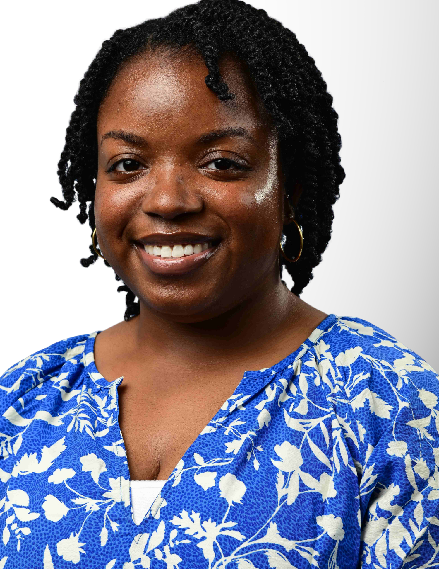 Smiling woman with braided hair wearing a blue floral blouse poses for a professional headshot photo.