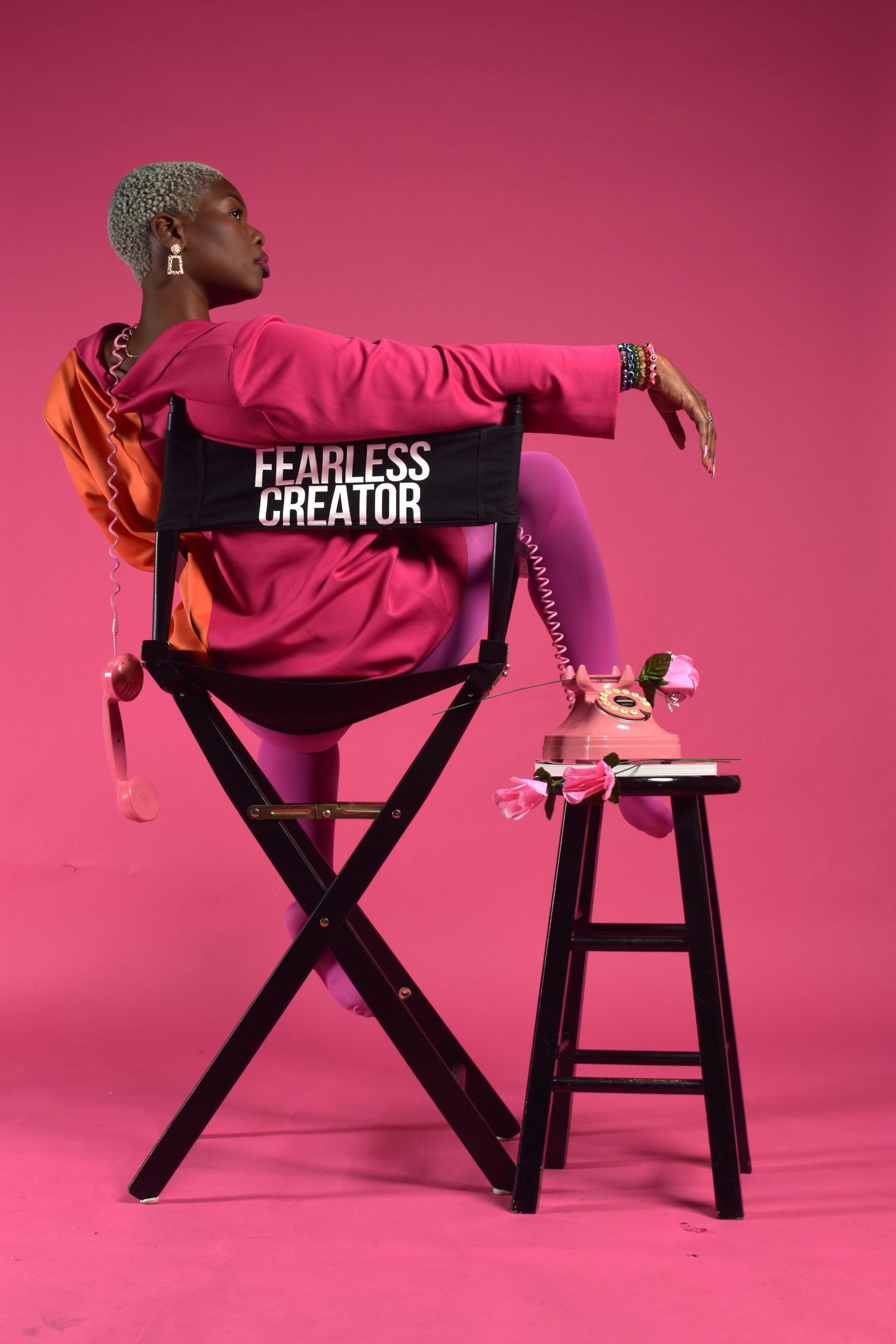 A Black woman in pink outfit sits in a director's chair labeled 'Fearless Creator' against a pink background.