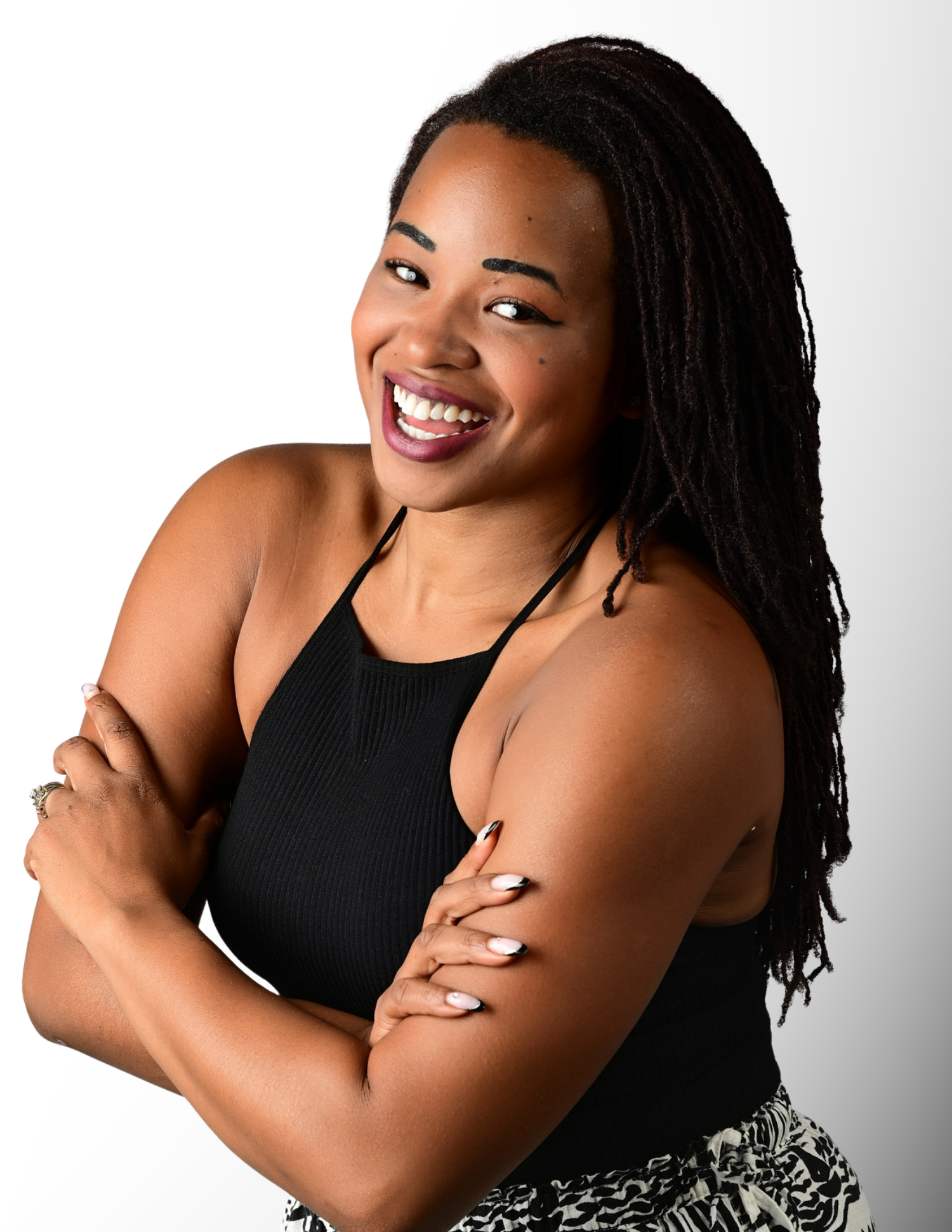 A smiling young Black woman with box braids poses confidently with arms crossed wearing a black sleeveless top.
