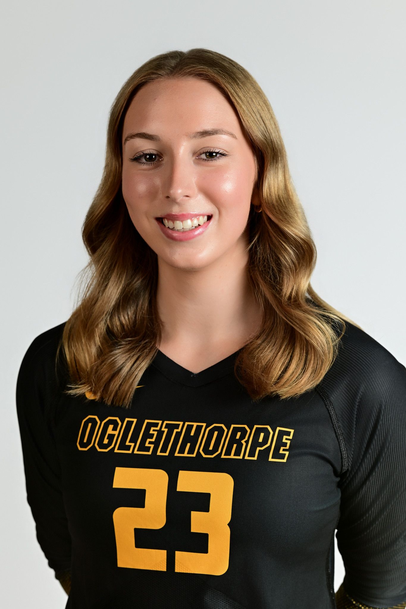 Oglethorpe University volleyball player wearing black and gold jersey number 23 poses for official team headshot photo.