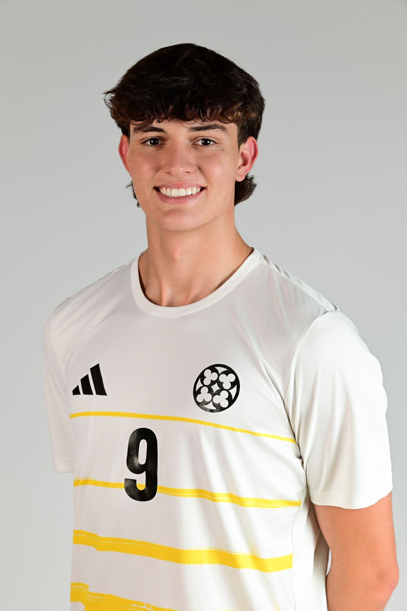 Young male soccer player wearing white Adidas jersey number 9 with yellow stripes, smiling for team portrait photo.