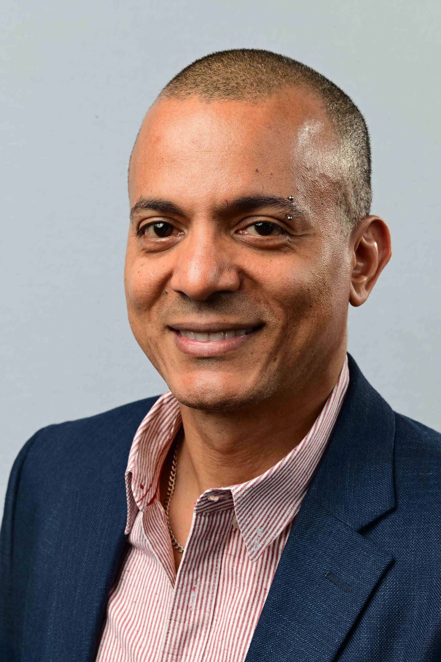Smiling middle-aged man in a blue blazer and pink striped shirt with short hair.