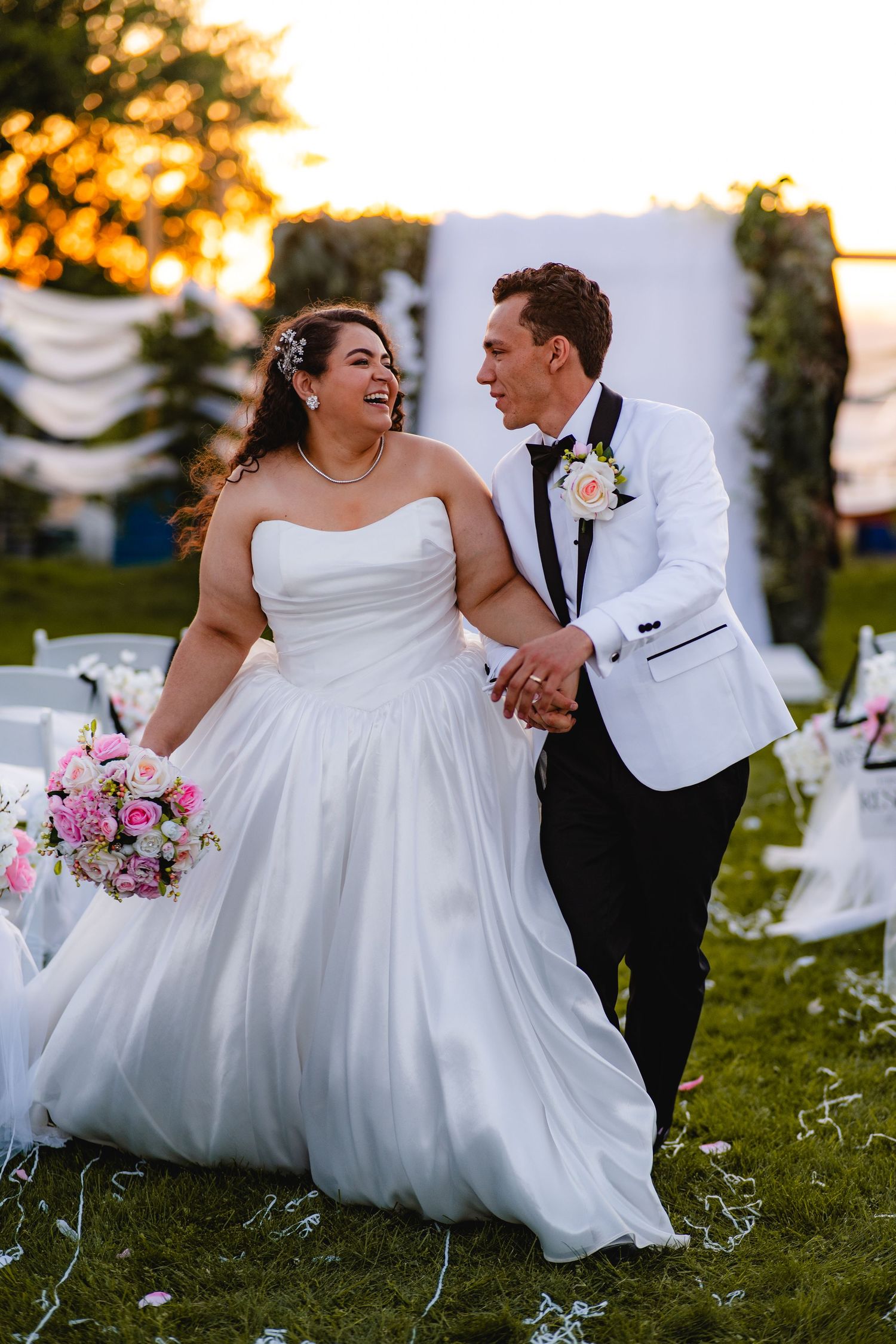 Bride and groom walking hand in hand outdoors at sunset wedding ceremony, bride holding pink bouquet at a backyard wedding in Chandler, AZ