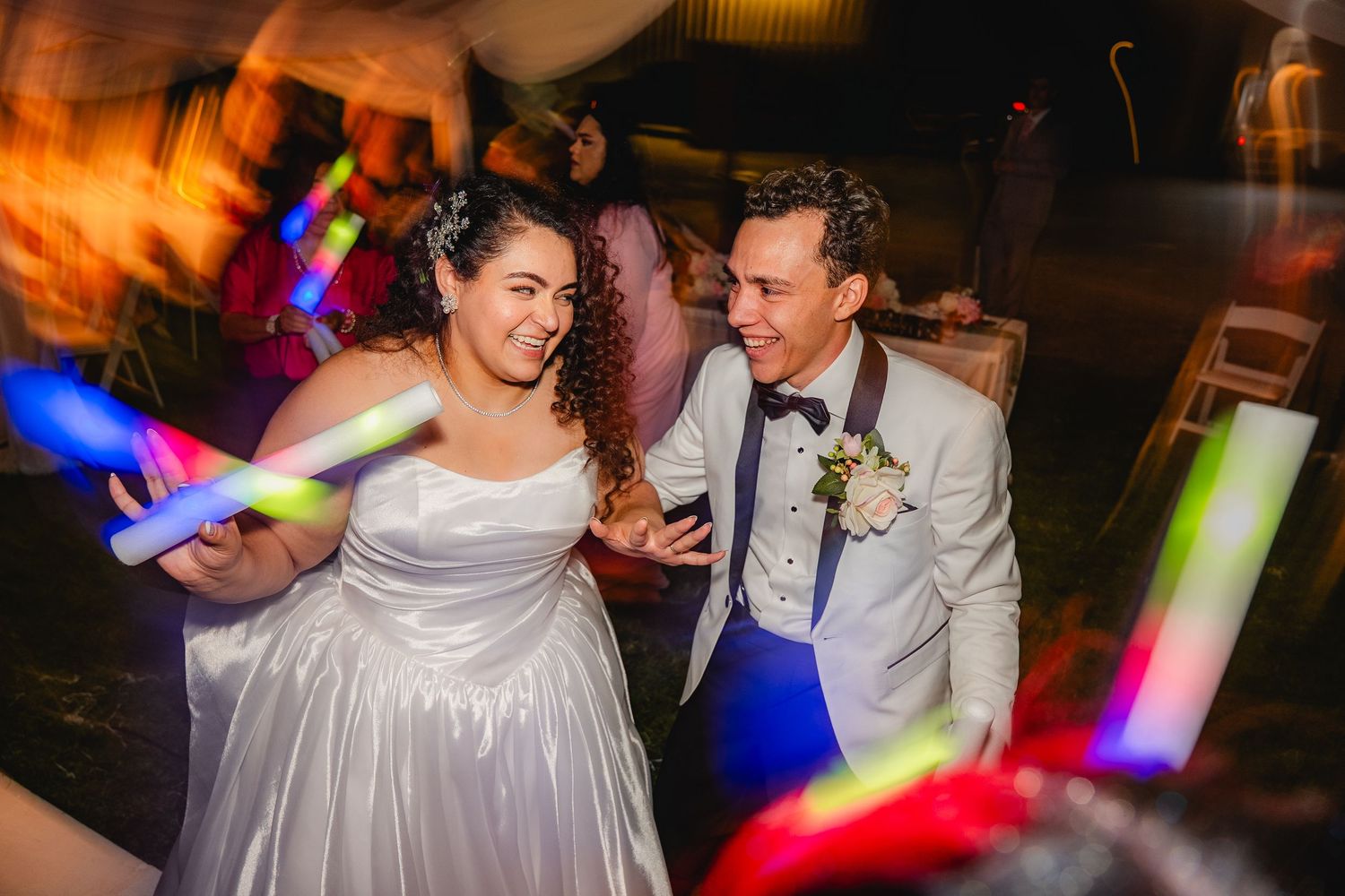 Bride and groom laughing together at. an Arizona wedding surrounded by colorful glowing light sticks at nightingale a shutter drag photo