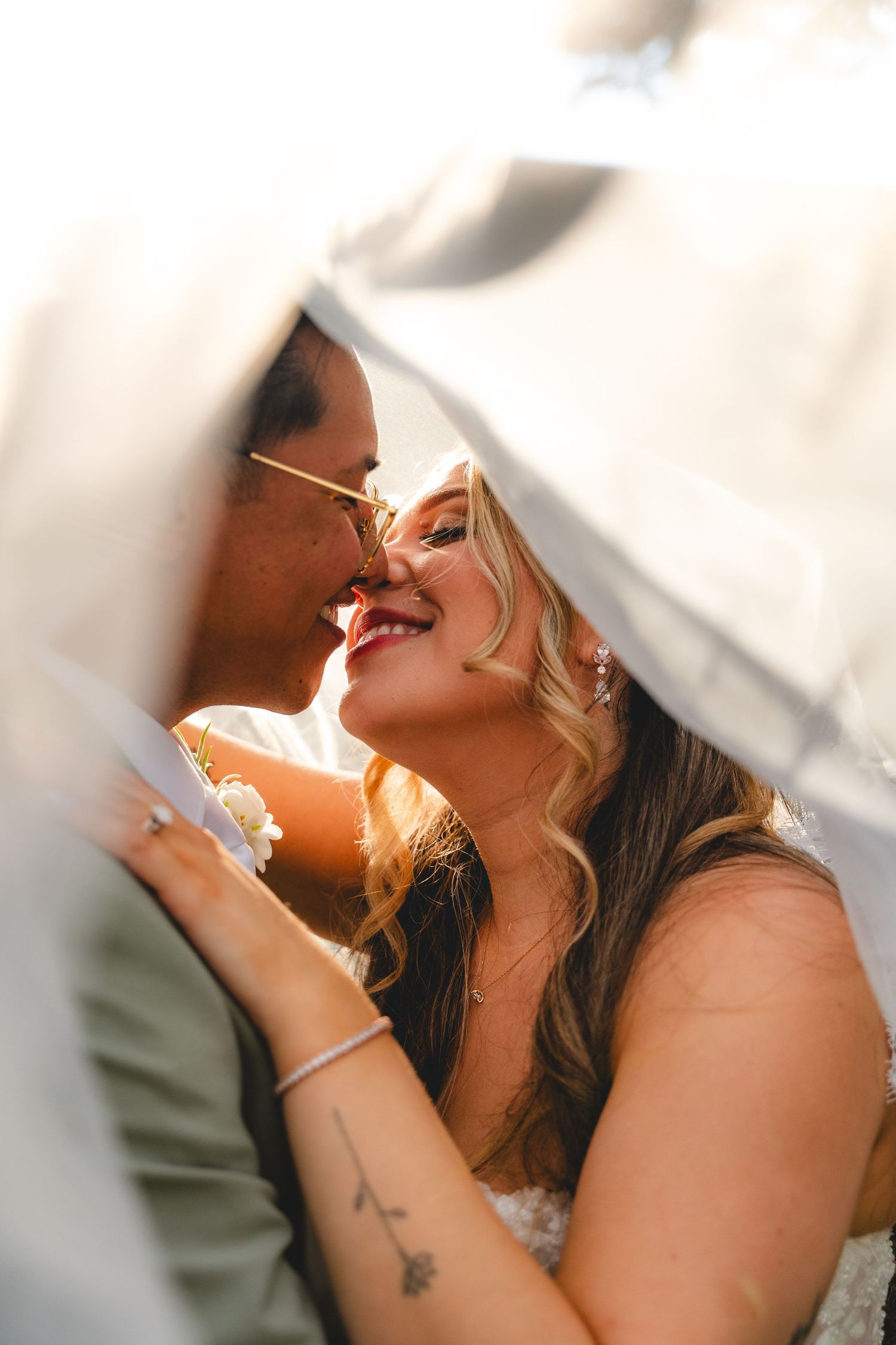 Bride and groom sharing a romantic kiss under a wedding veil in golden sunlight at a San Diego Wedding at The Handlery Hotel