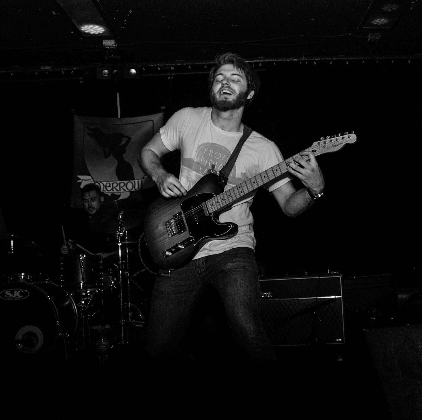 Black and white photo of a male guitarist jumping on stage during a live rock concert performance.