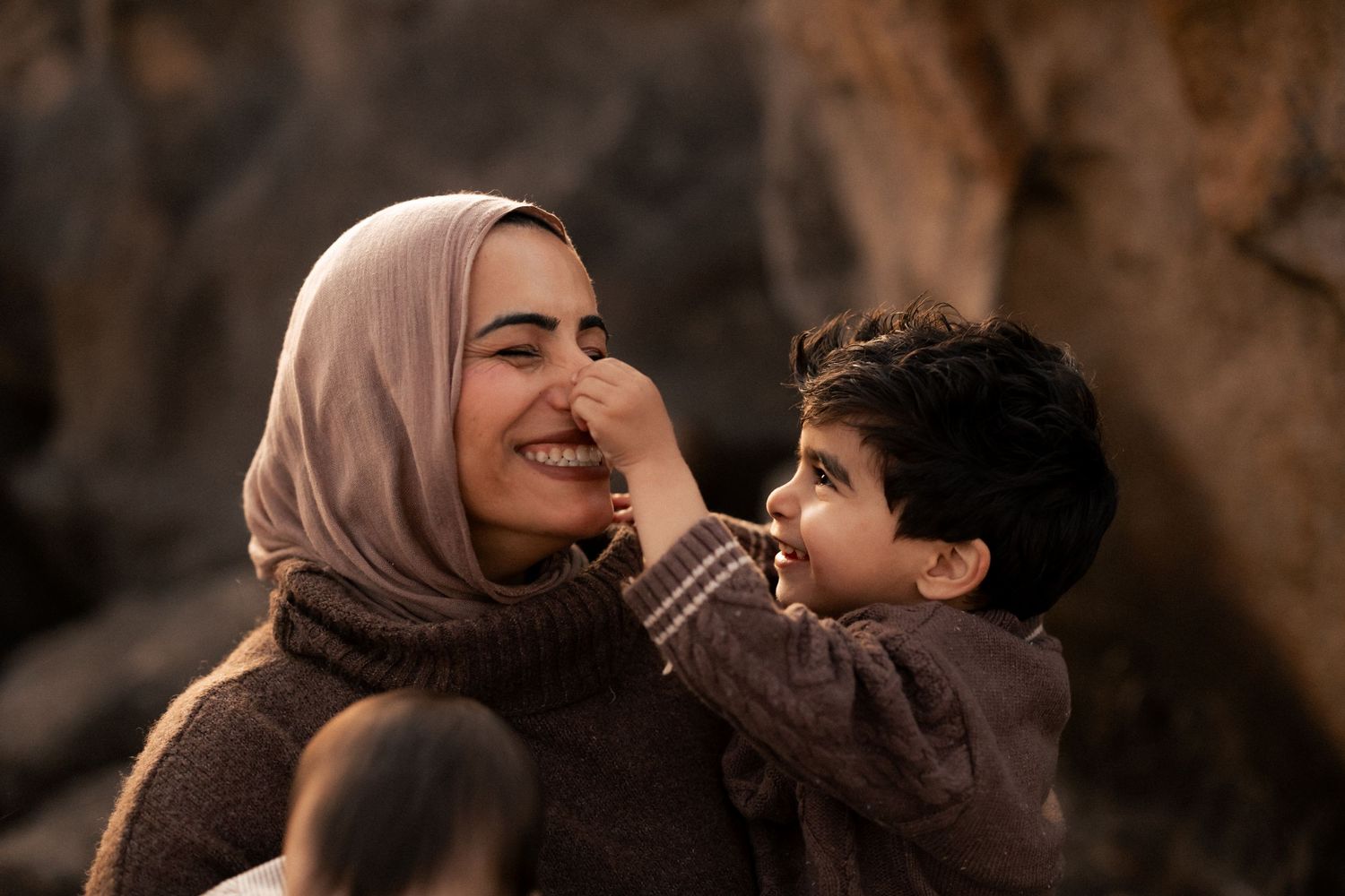 A smiling woman in a hijab shares a joyful moment with a young child touching her nose outdoor at sunset golden hour