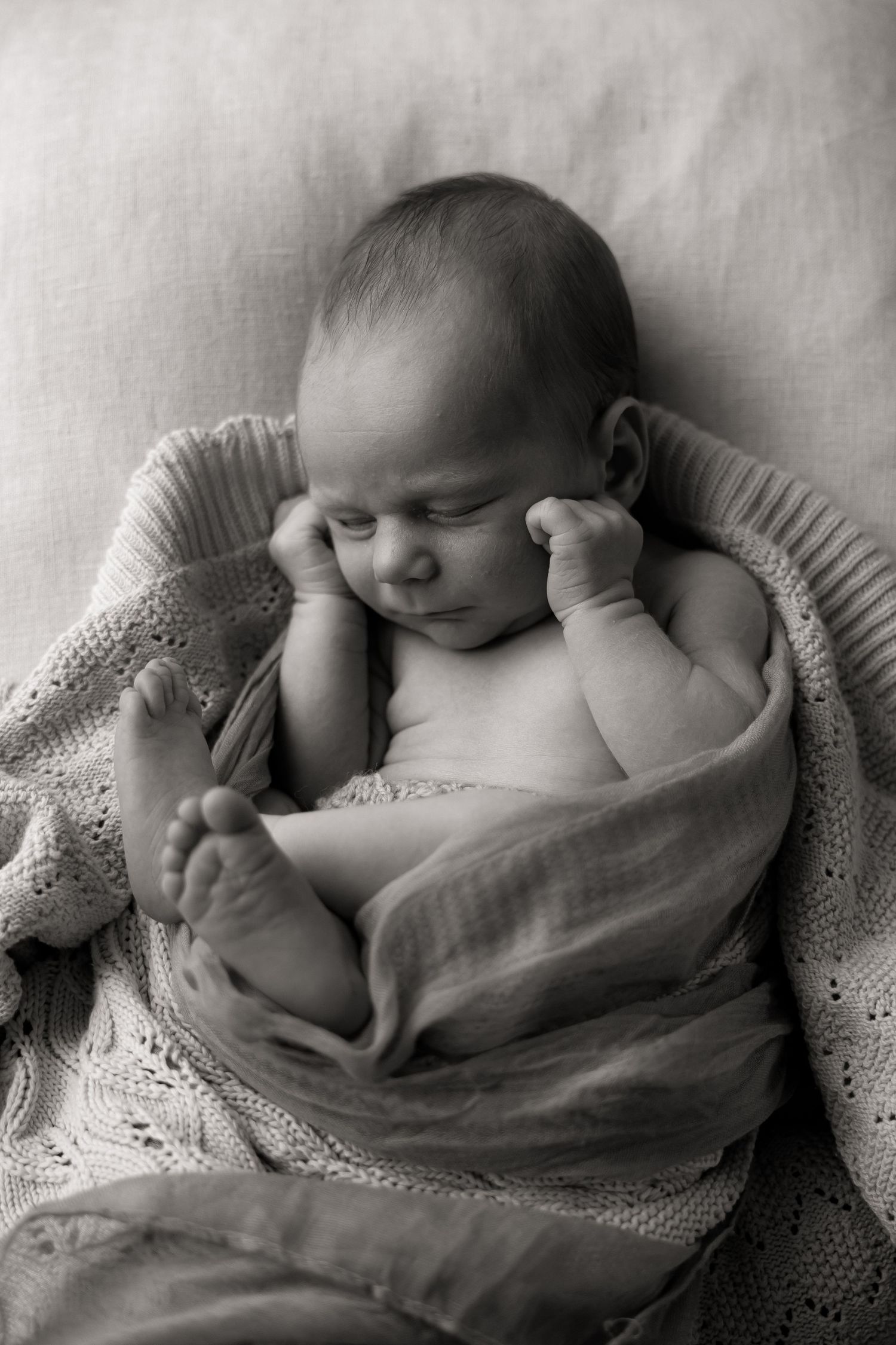 A closeup photo of a newborn baby cuddled up in blankets in a mundaring studio setting