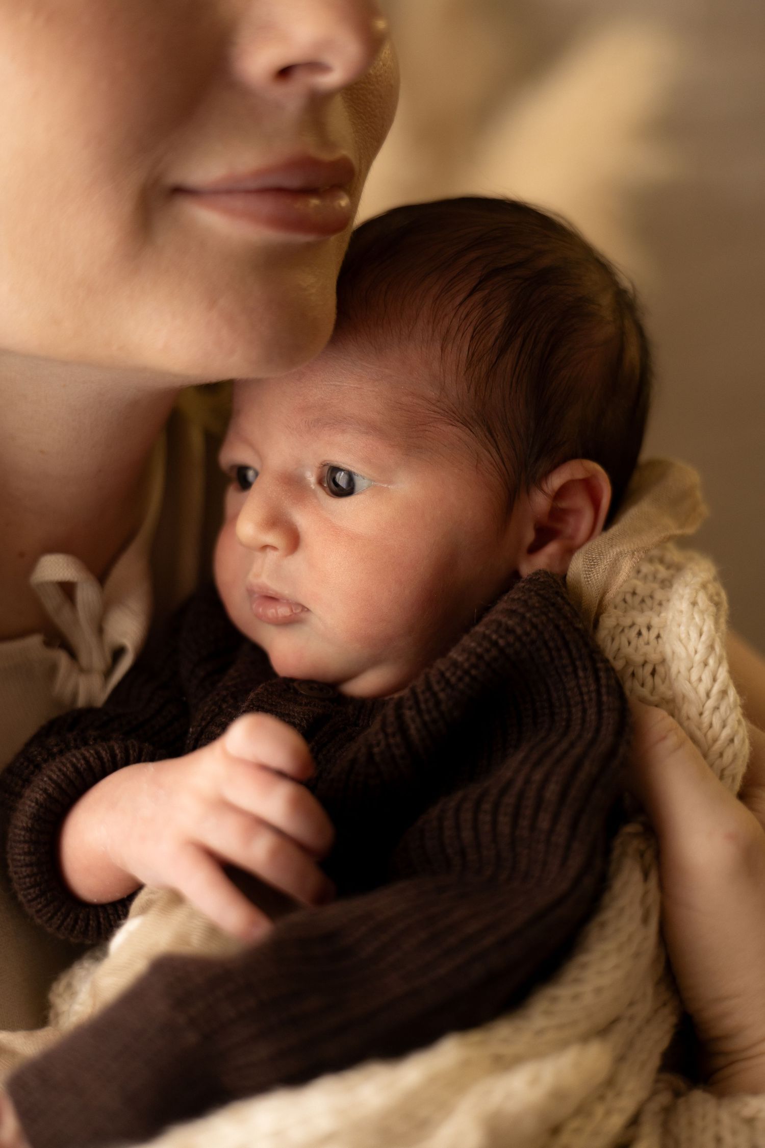 A mother tenderly holds her newborn baby wrapped in a brown knit blanket, capturing an intimate bonding moment.