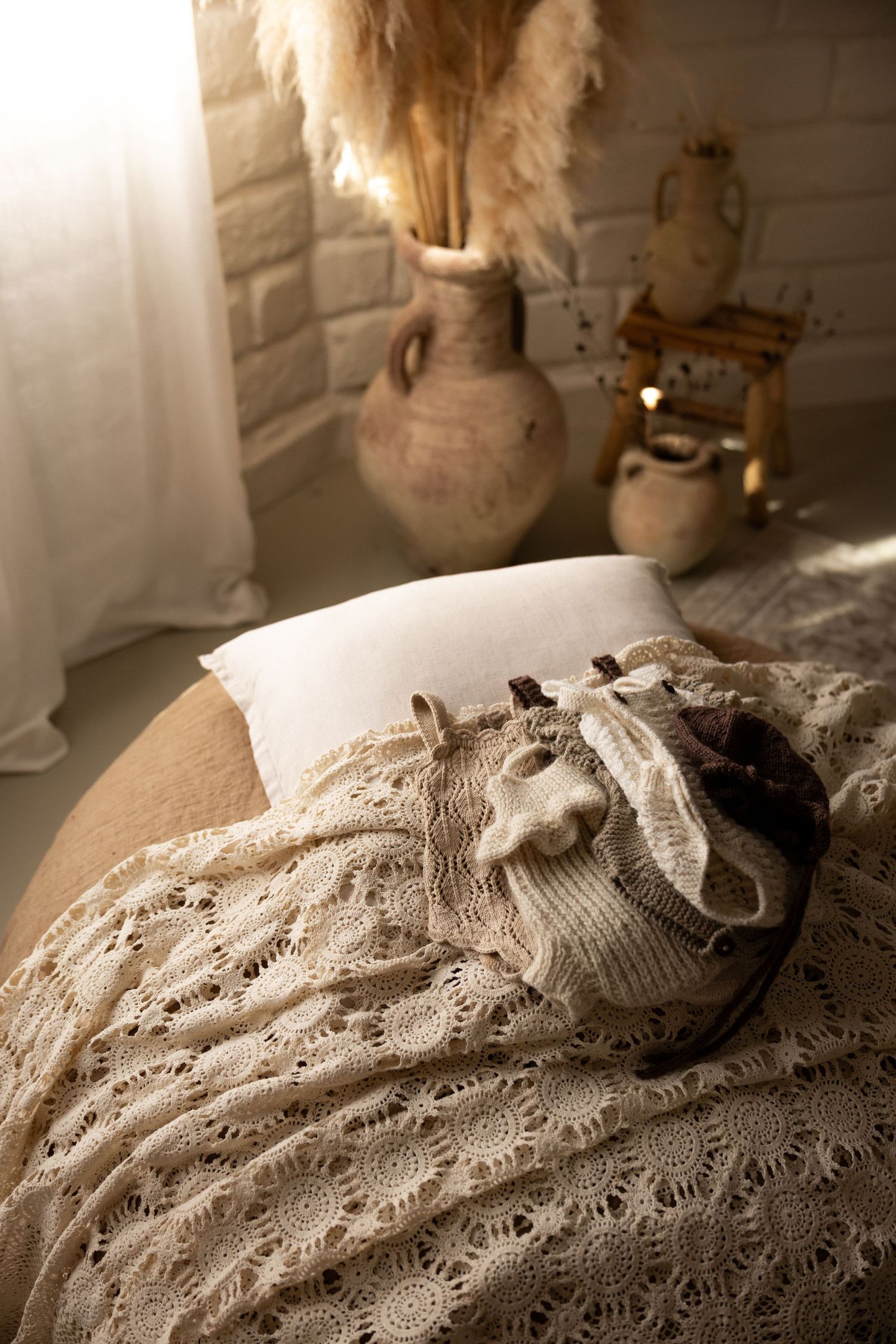 Cozy boho bedroom with crochet lace blanket, knit accessories, ceramic vases, and pampas grass in warm sunlight.