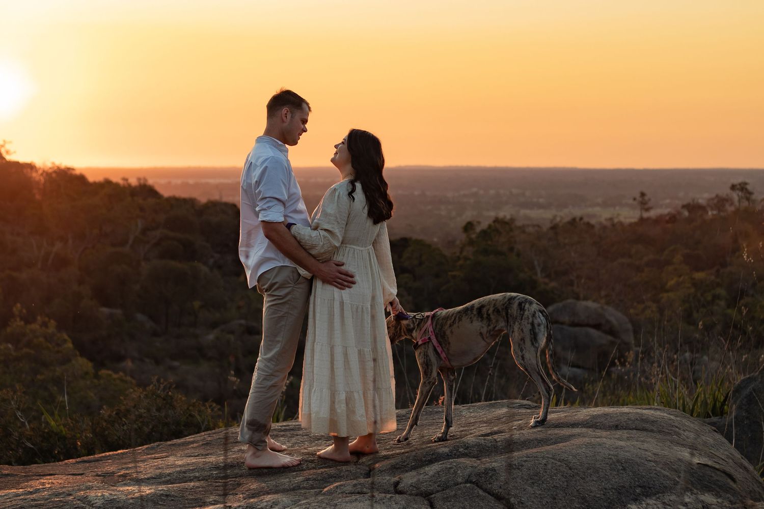 A couple and their dog overlook a beautiful view backdrop in the Perth hills at sunset golden hour