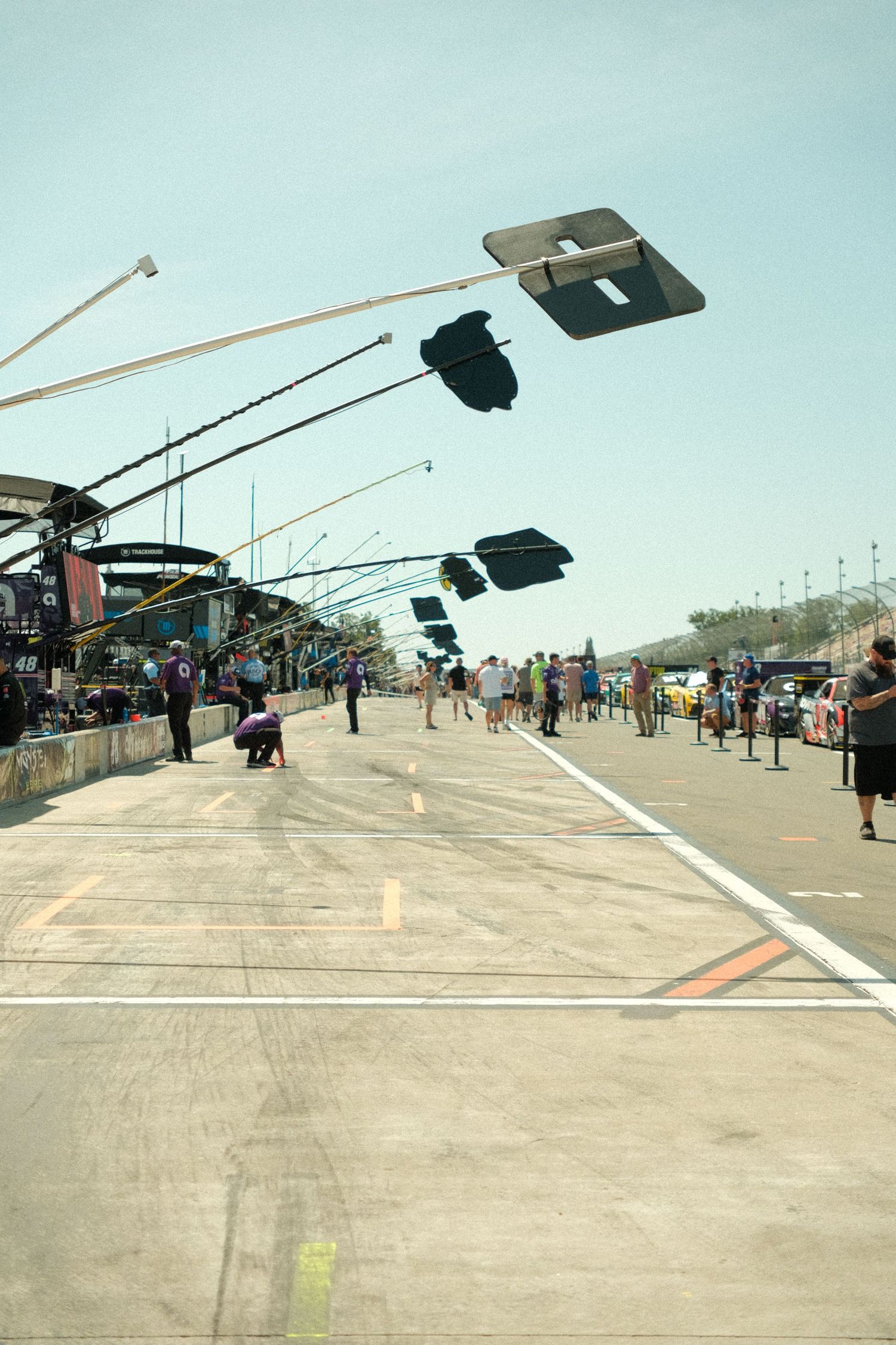 Wide view of a NASCAR pit lane with signal boards extended over the road on a clear day.
