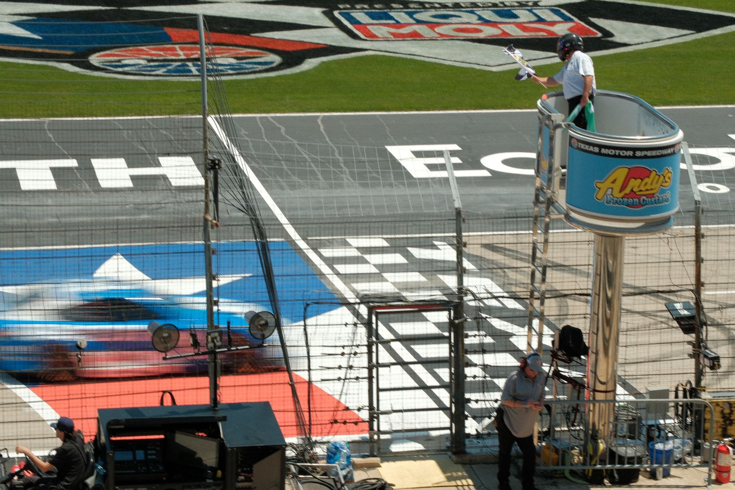Track workers paint colorful sponsor logos and graphics on a NASCAR race track surface before an event.
