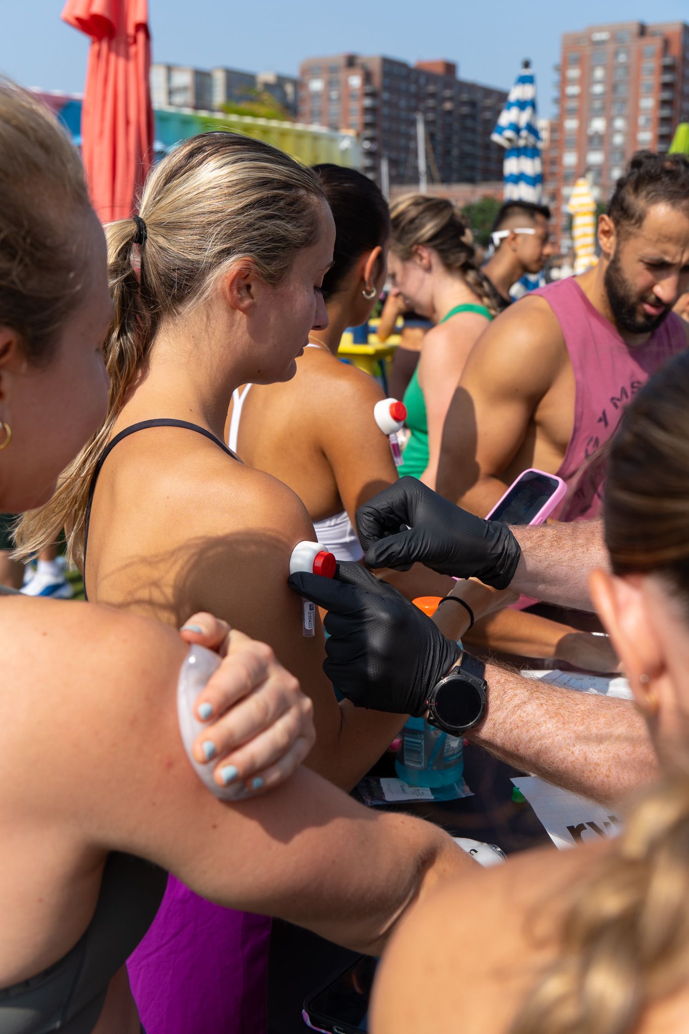 Fitness event volunteers writing race numbers on participants arms at outdoor athletic competition.
