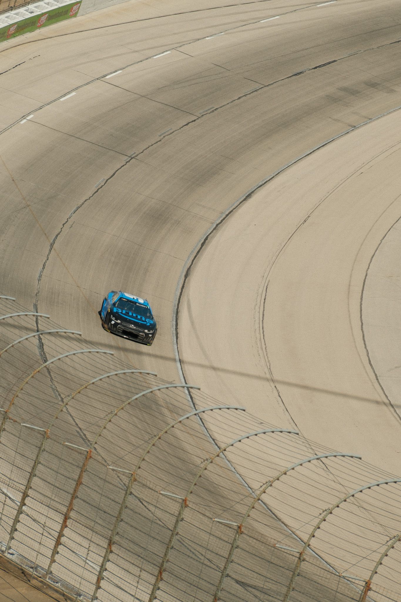 Aerial view of blue NASCAR race car navigating banked turn at high-speed oval track.