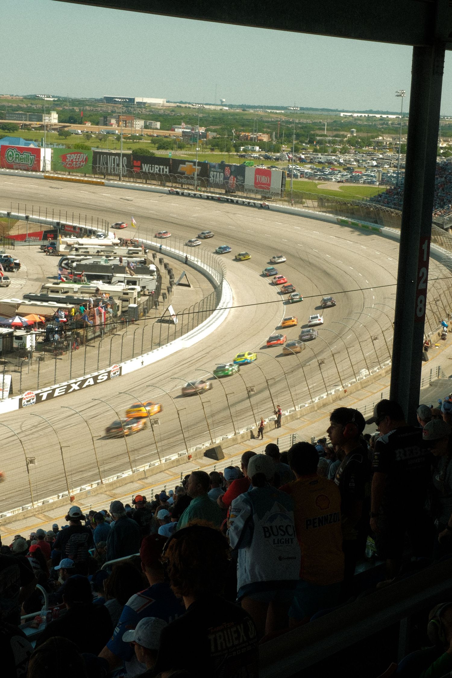Aerial view of NASCAR stock cars racing on the banked oval track at Texas Motor Speedway before a packed crowd.