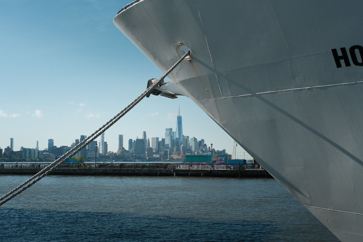 The bow of a large cargo ship with the New York City skyline and One World Trade Center in background from Hoboken, NJ.